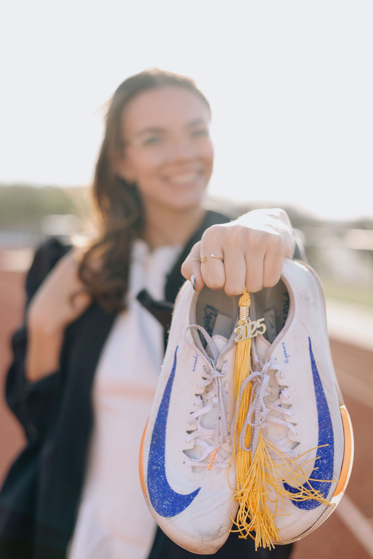 White sneakers with blue details and gold tassels held up against a bright background.