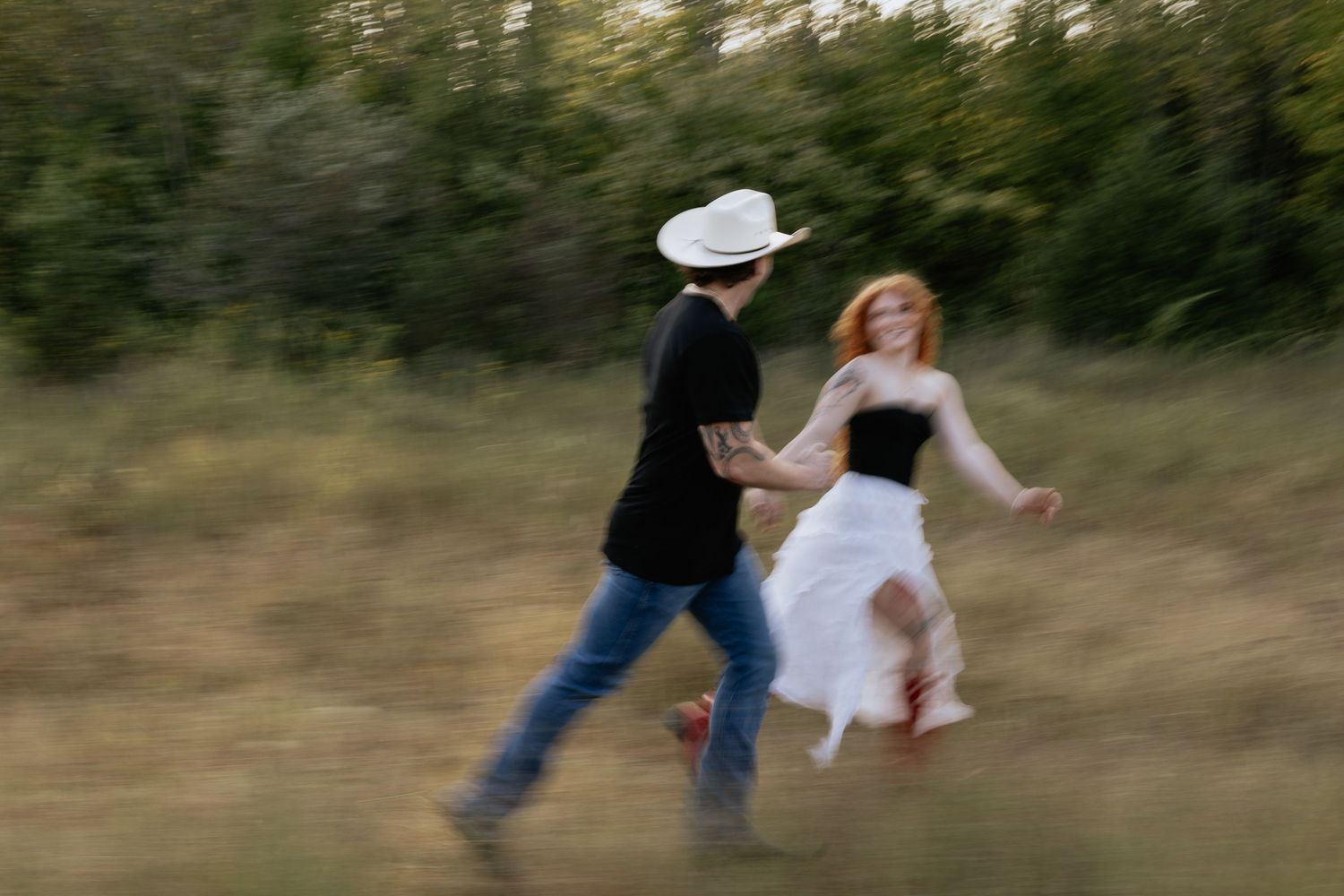 A playful couple tumbles down a grassy hillside at sunset.