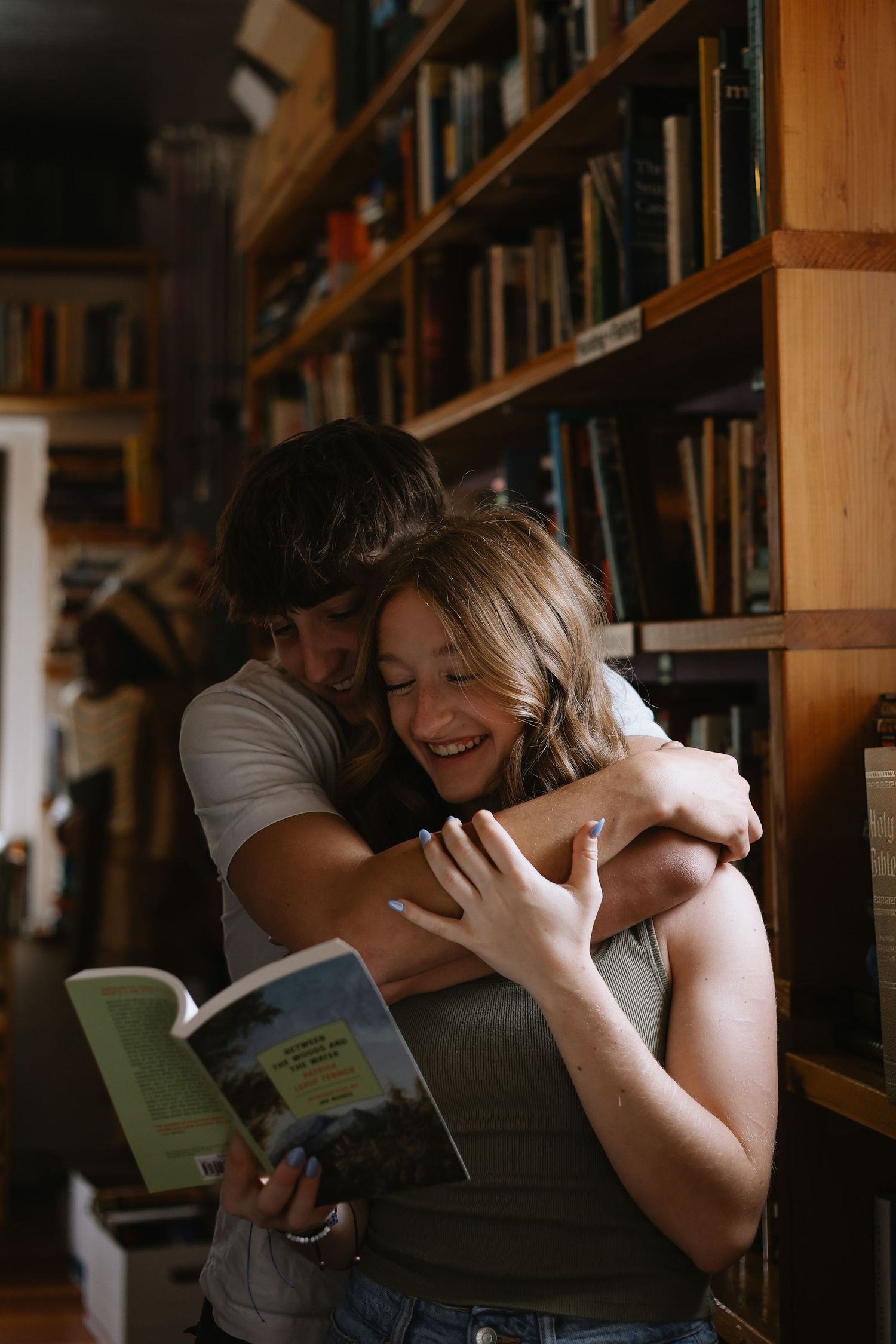 Couple sharing intimate moment between library bookshelves.