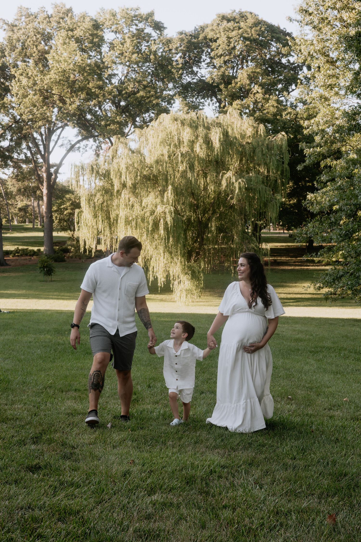 A family shares tender moments together on a grassy lawn with weeping willow trees in the background.