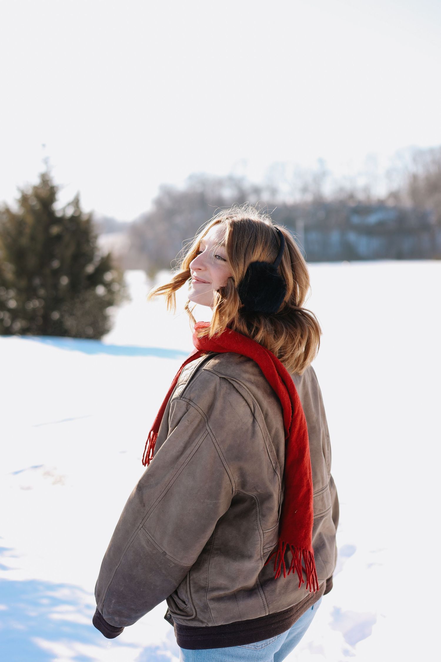 Candid winter scene with person in brown coat and red scarf enjoying snowy landscape.