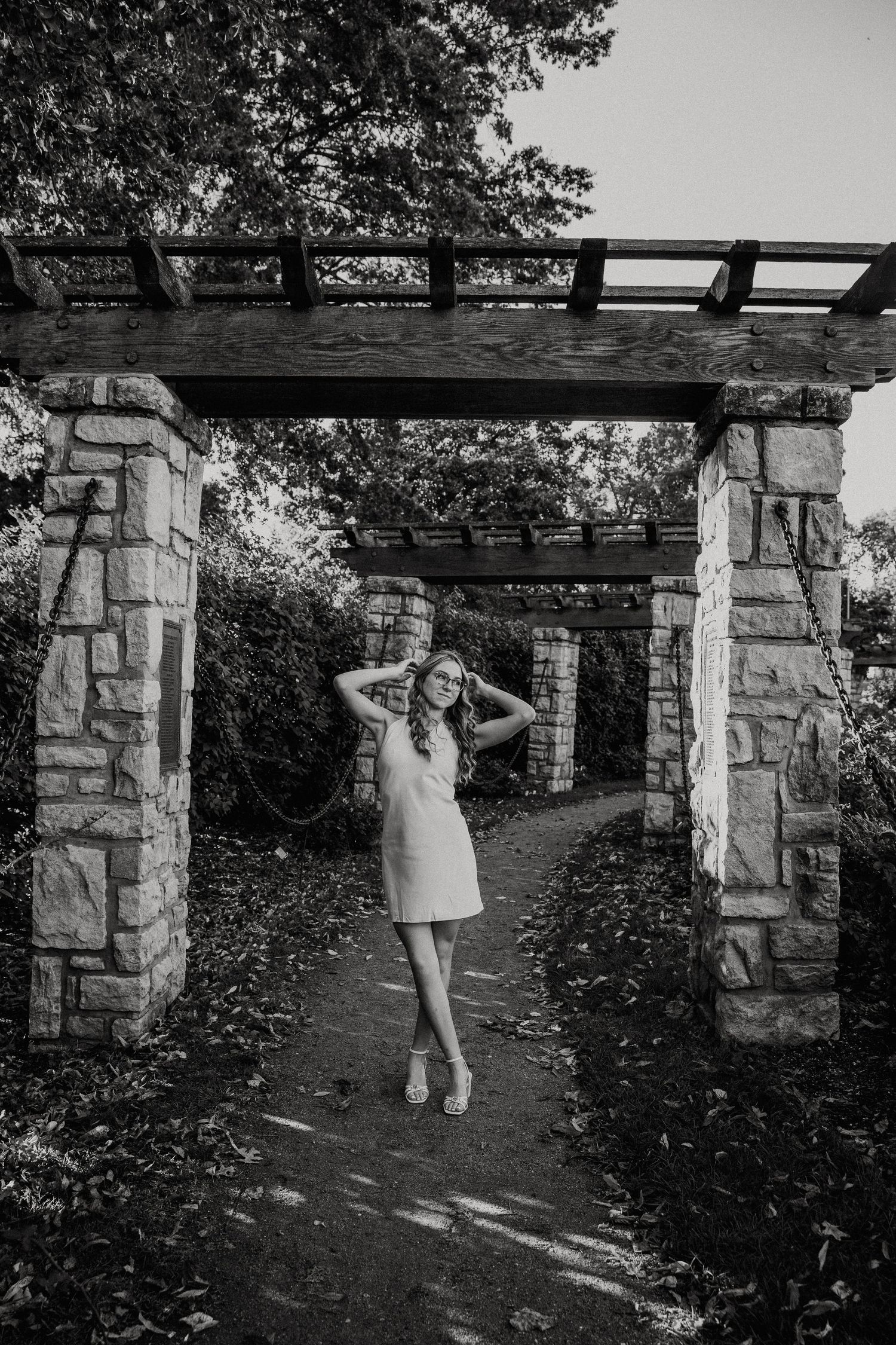 Black and white photo of girl posing with both hands in her hair looking off to the distance.