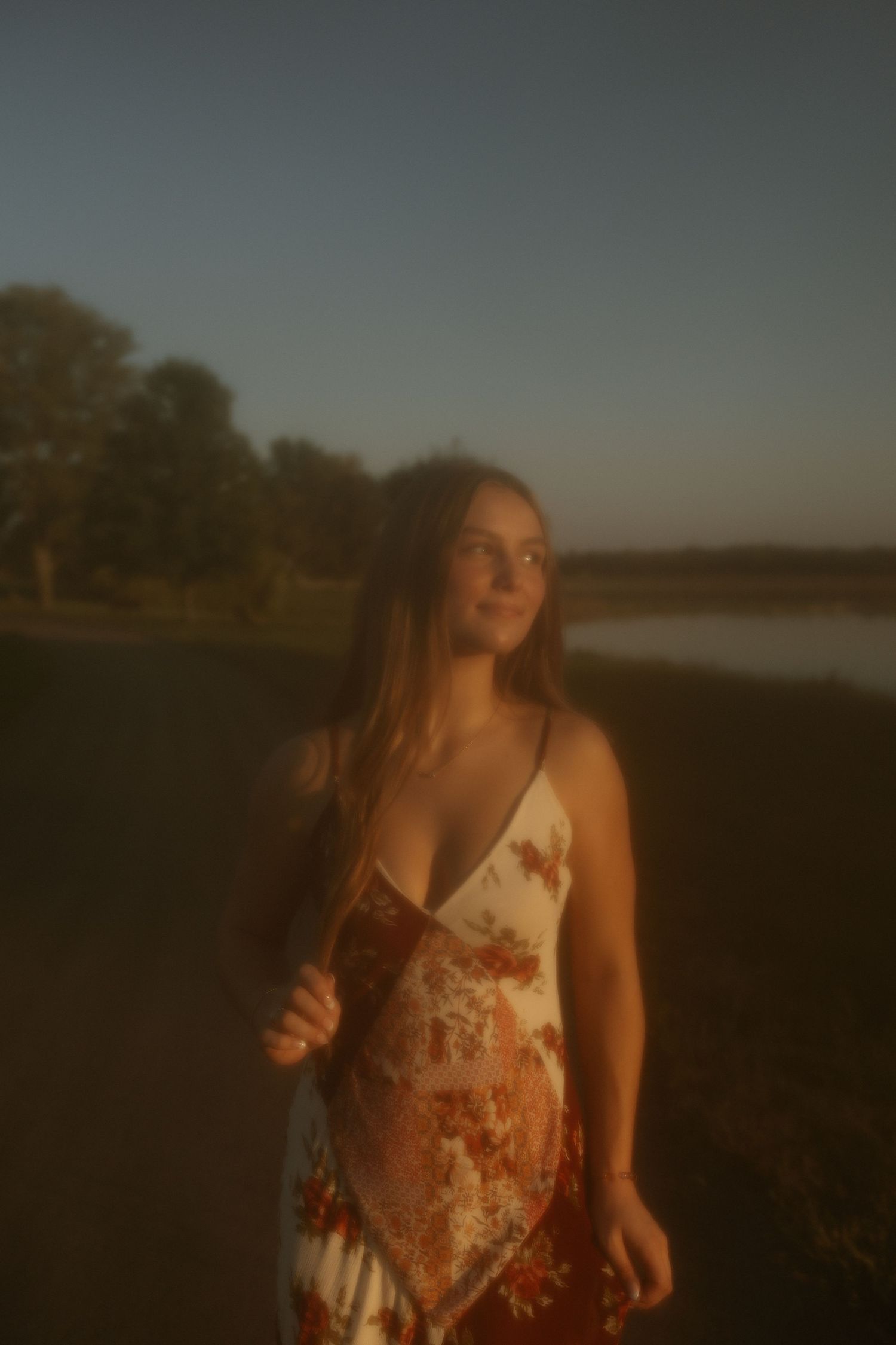 A moody sunset portrait in a floral dress by a lake.