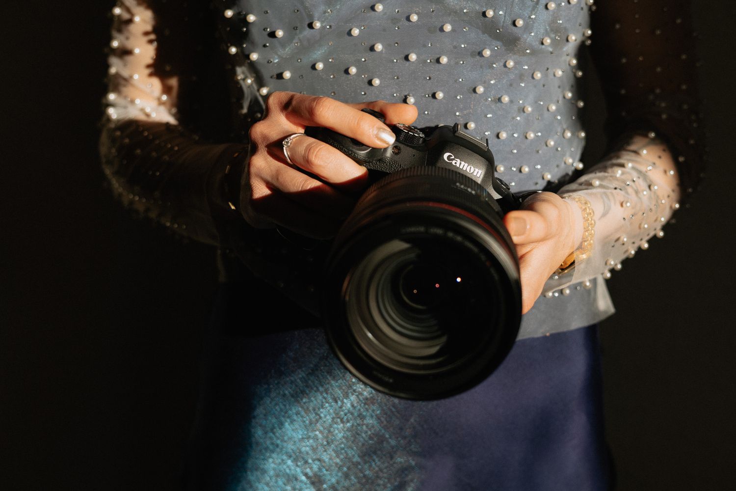 Hands holding black DSLR camera against blue sparkly fabric.