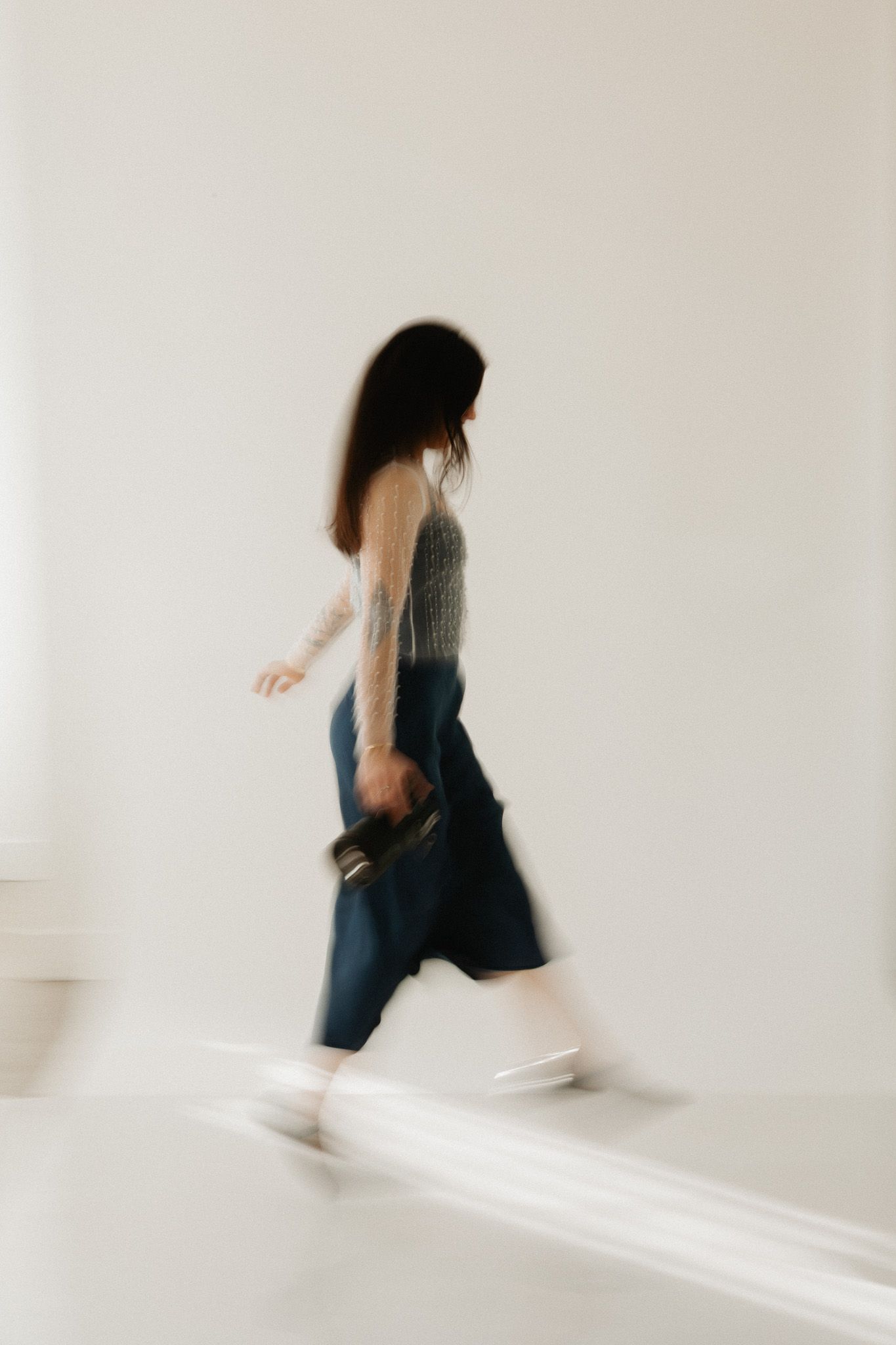 Motion blur photo of person walking past white wall in casual attire.