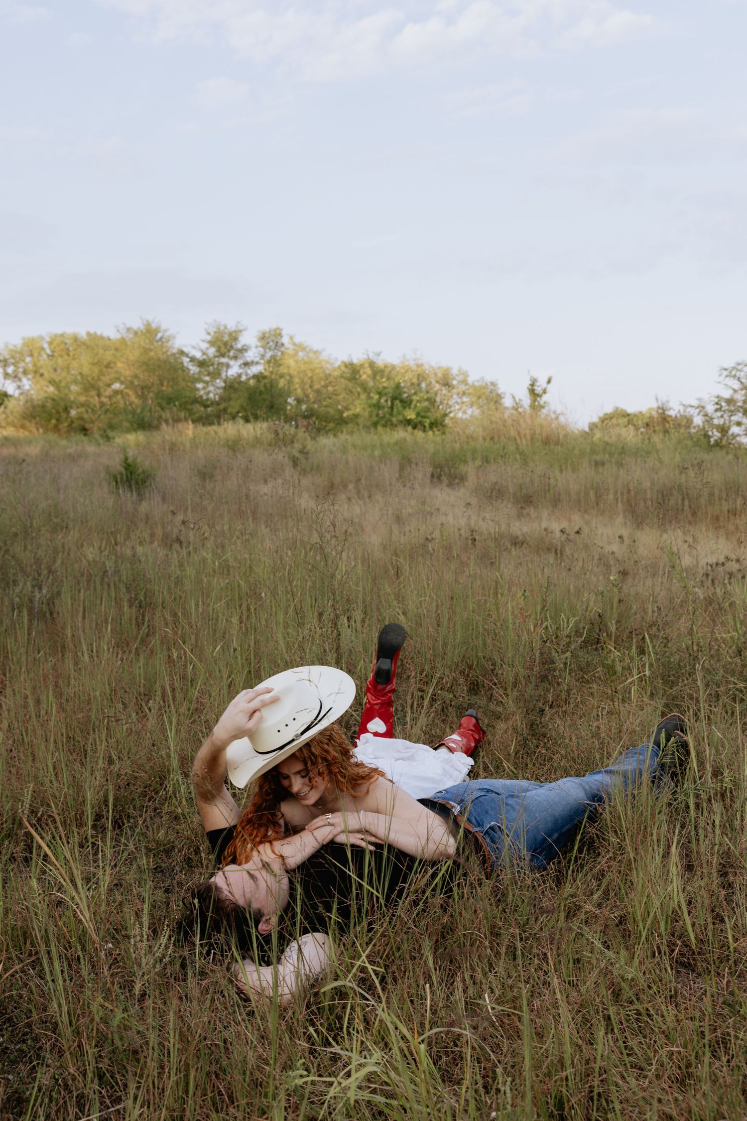 Two people lying down and laughing together in tall grass on a hillside.