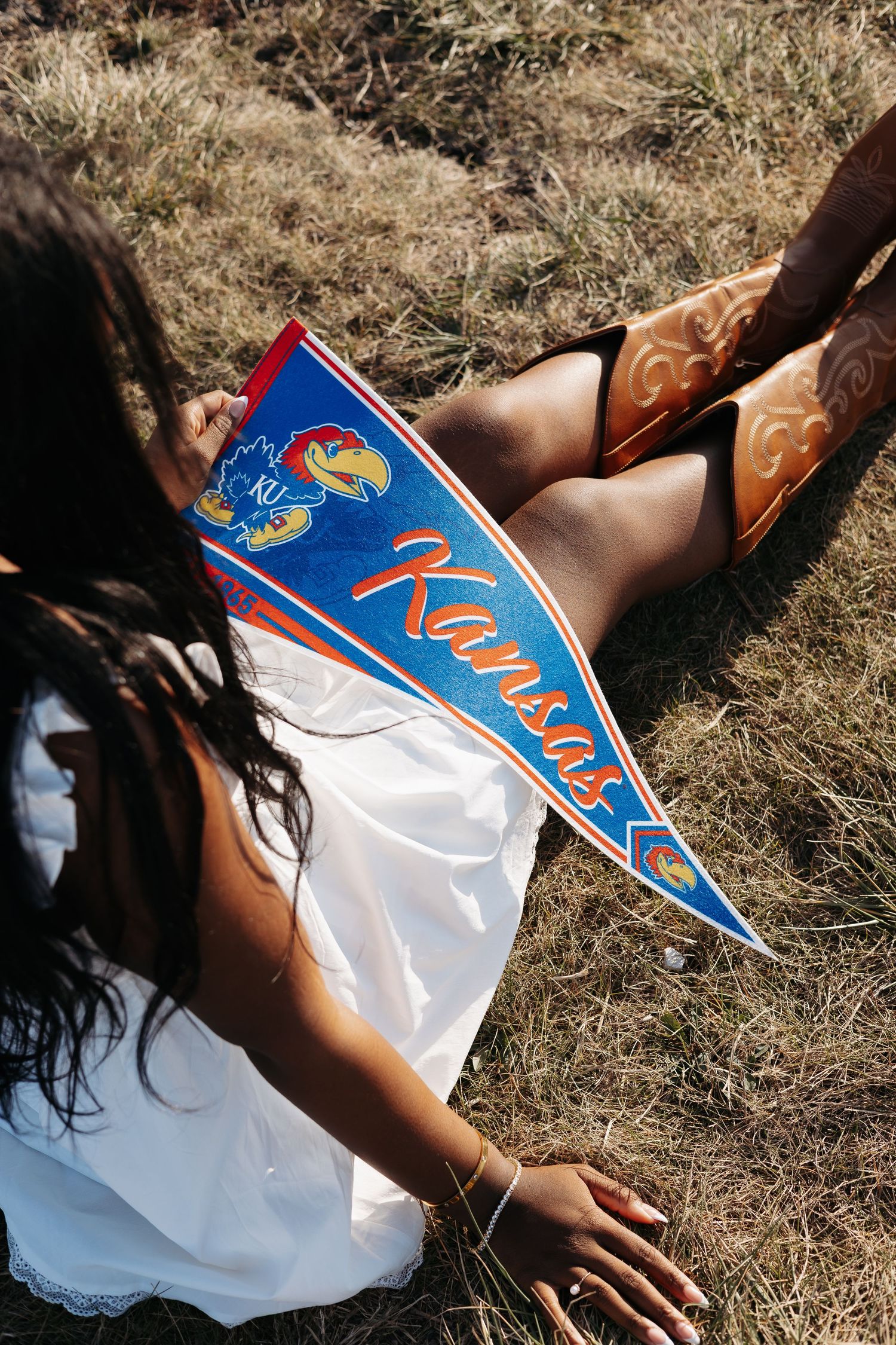 Blue and red Kansas Jayhawks pennant across girl's lap outside.