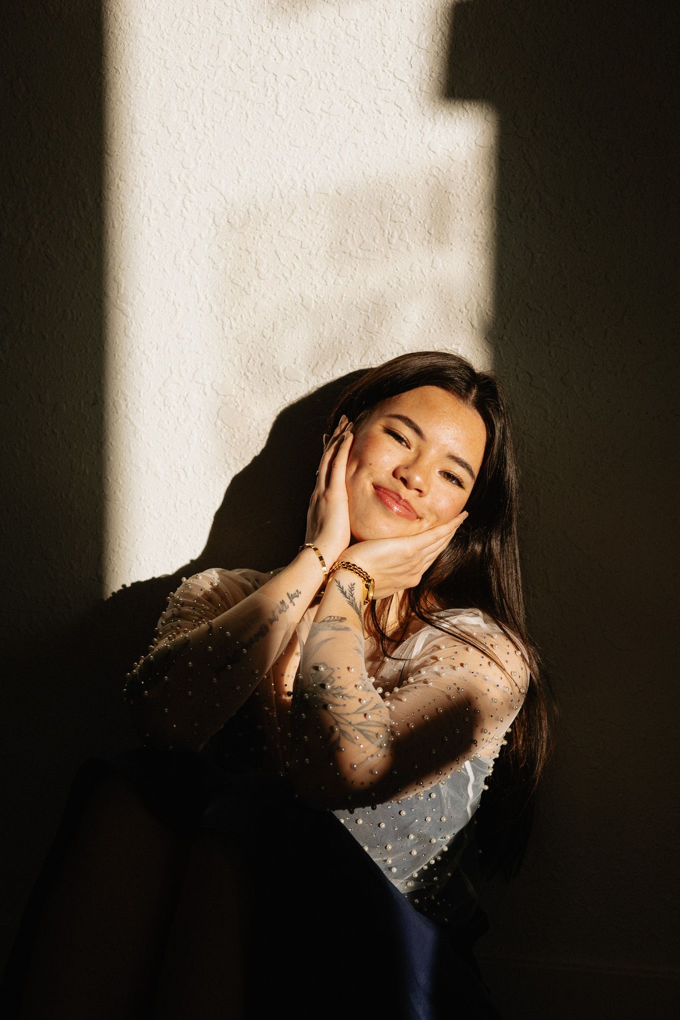 Dramatic portrait with sunlight and shadows creating moody atmosphere against white wall.