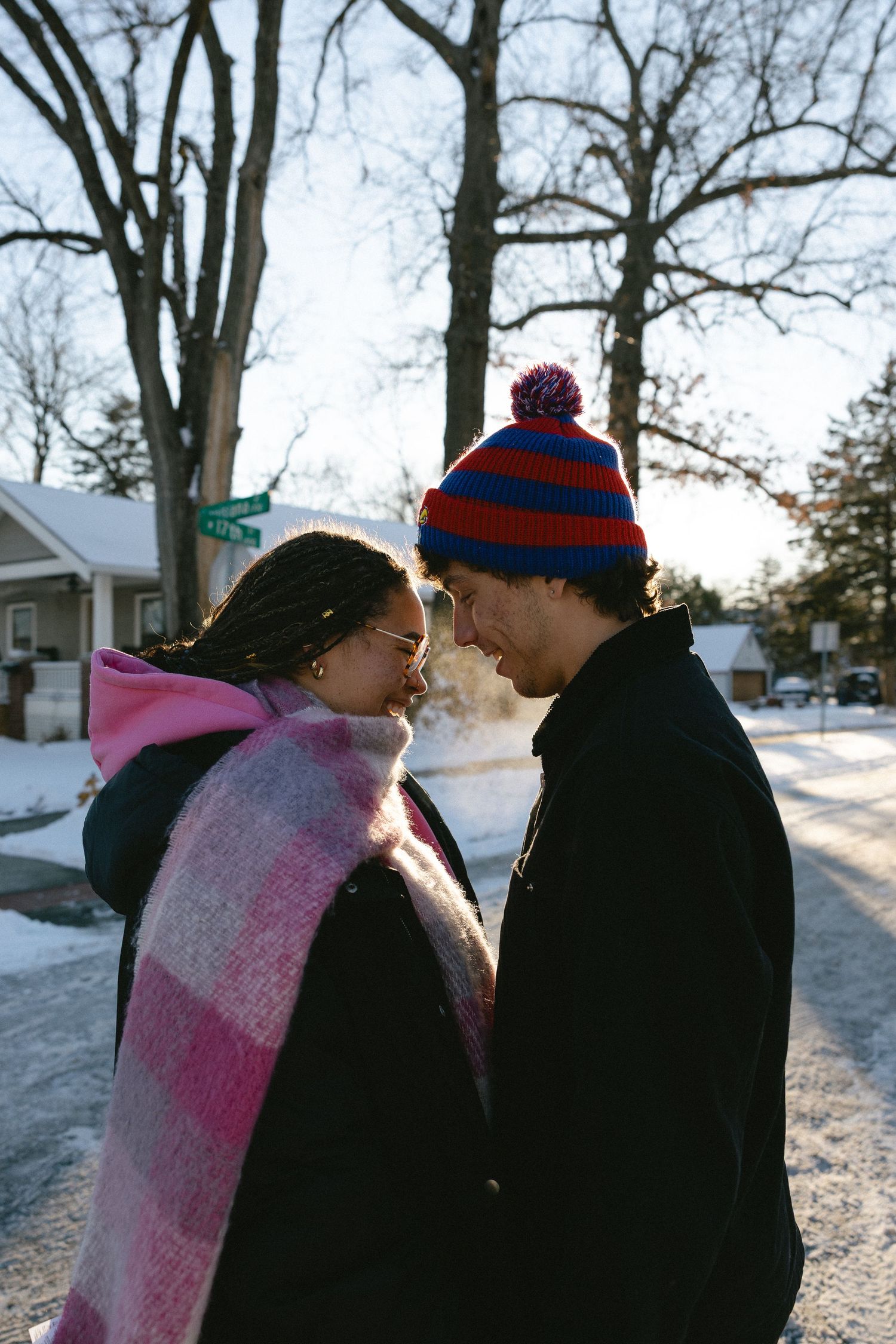 A couple wearing winter hats share an intimate moment in a snowy outdoor setting at dusk.