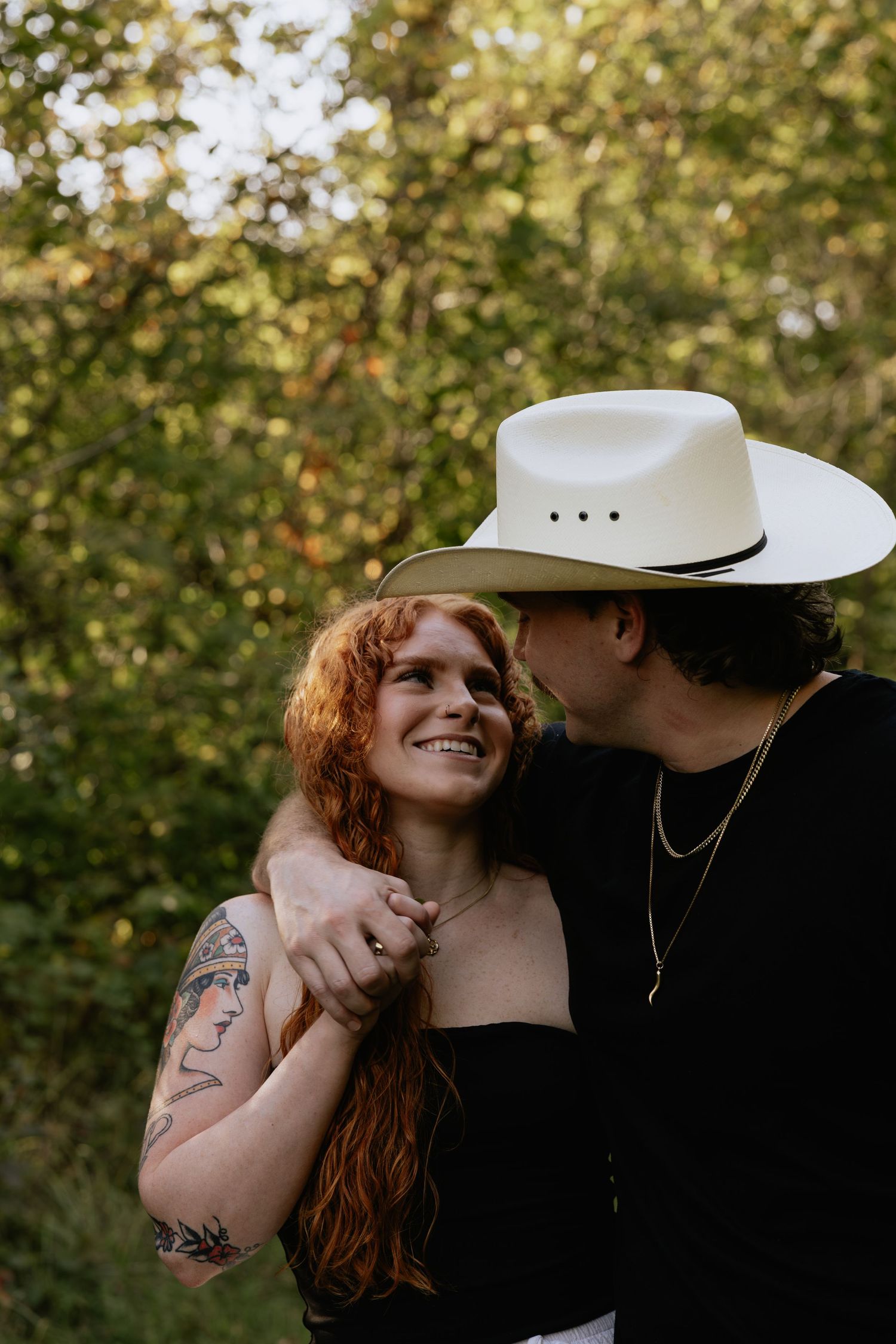 A romantic couple embraces outdoors with sunlit trees in the background during a golden hour photoshoot.