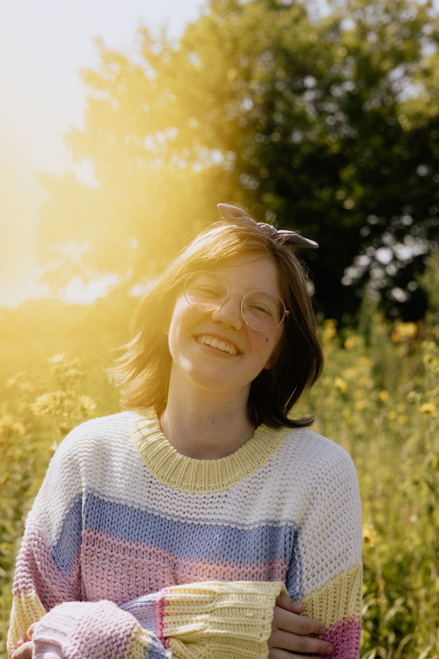 Joyful moment captured in sunlit field wearing pastel knit sweater.