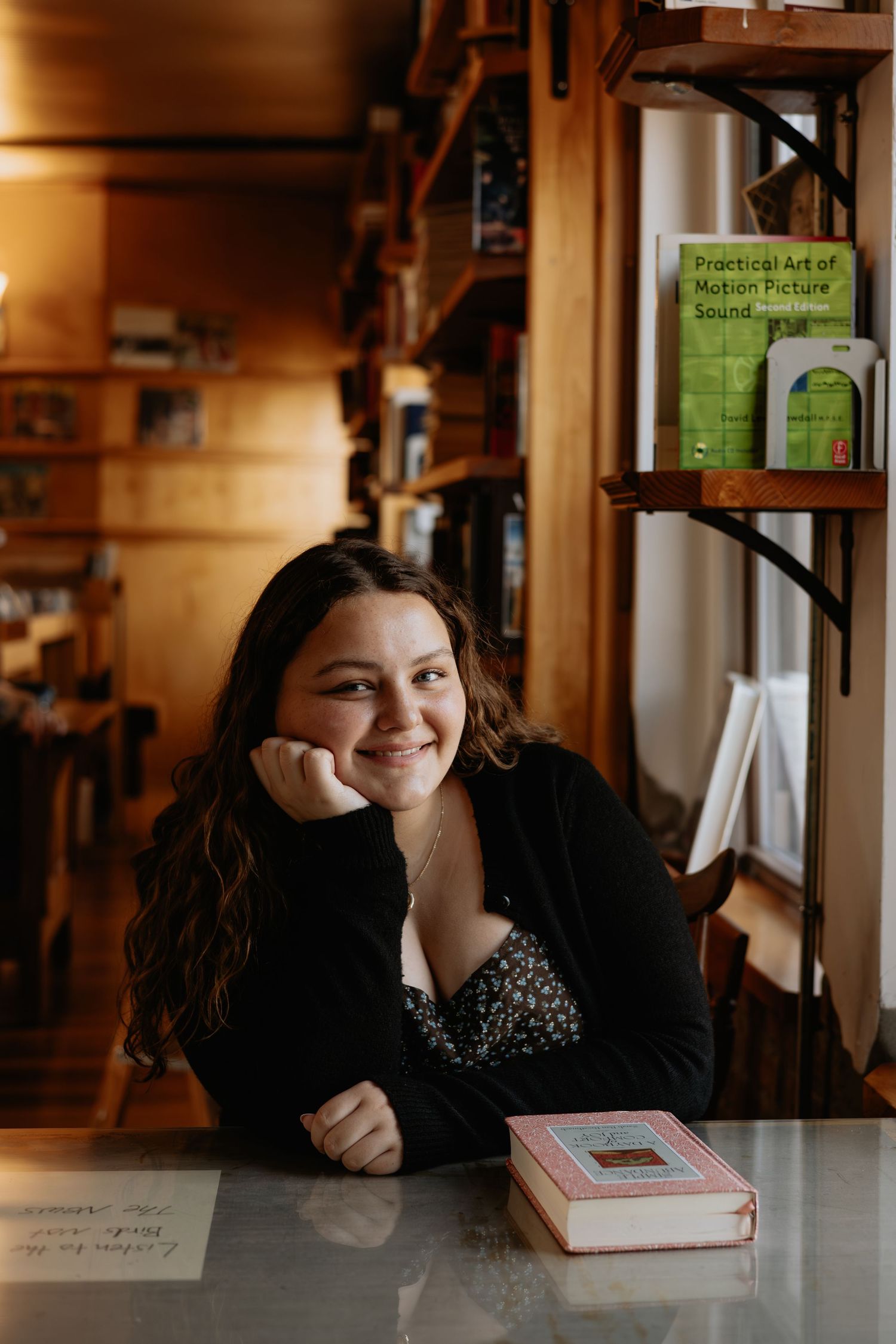 A cozy indoor portrait at a desk with bookshelves in warm lighting.