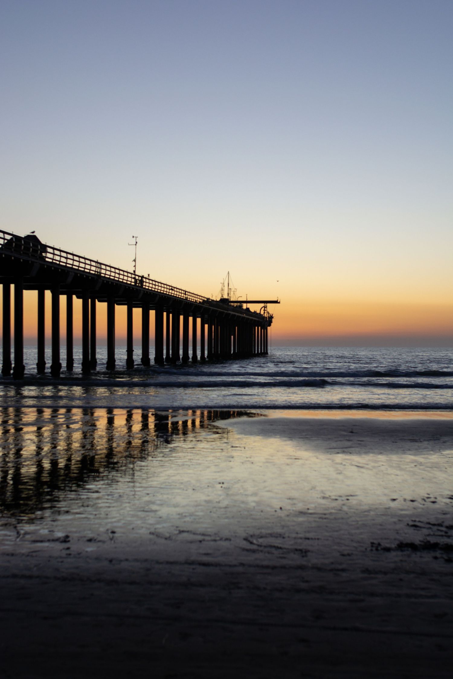 The Scripps Pier at La Jolla Shores Beach during sunset, showcasing the fading sunlight and dimming ocean.