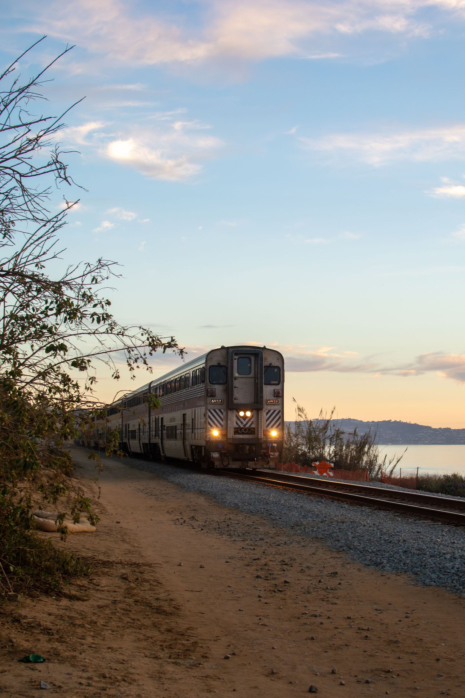 A train in Del Mar approaches the viewer at evening time, framed by the fading sun in the background above the ocean.
