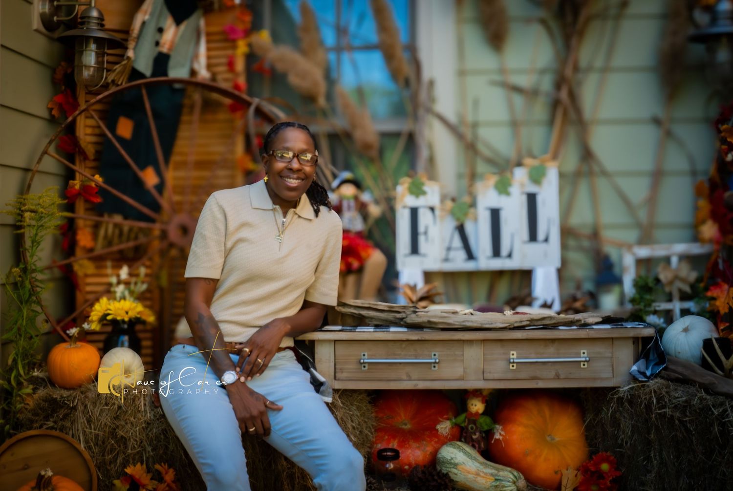 Fall themed photo shoot setup with hay bales, pumpkins, and autumn decorations against a rustic blue barn wall.