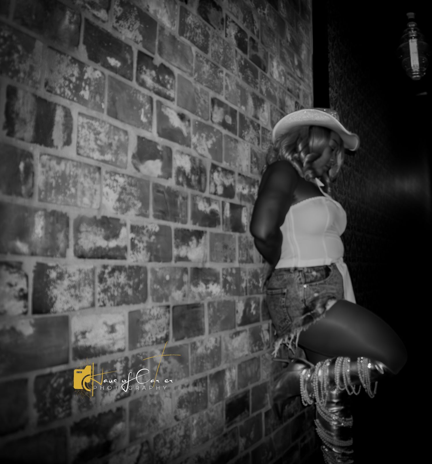 Dramatic black and white portrait against textured brick wall with moody lighting.
