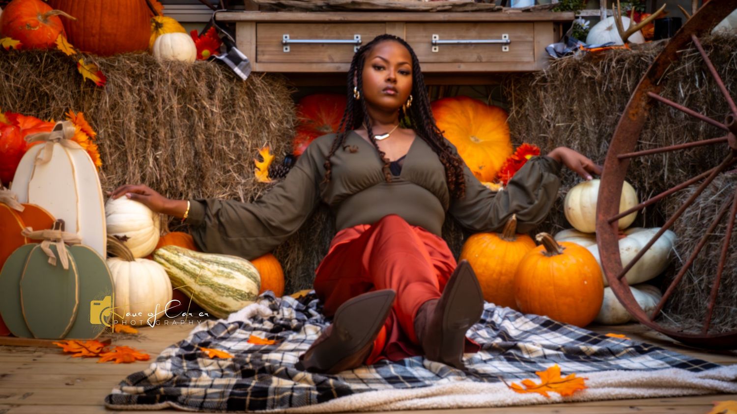 Row of orange and white pumpkins arranged on plaid blanket with hay bales.