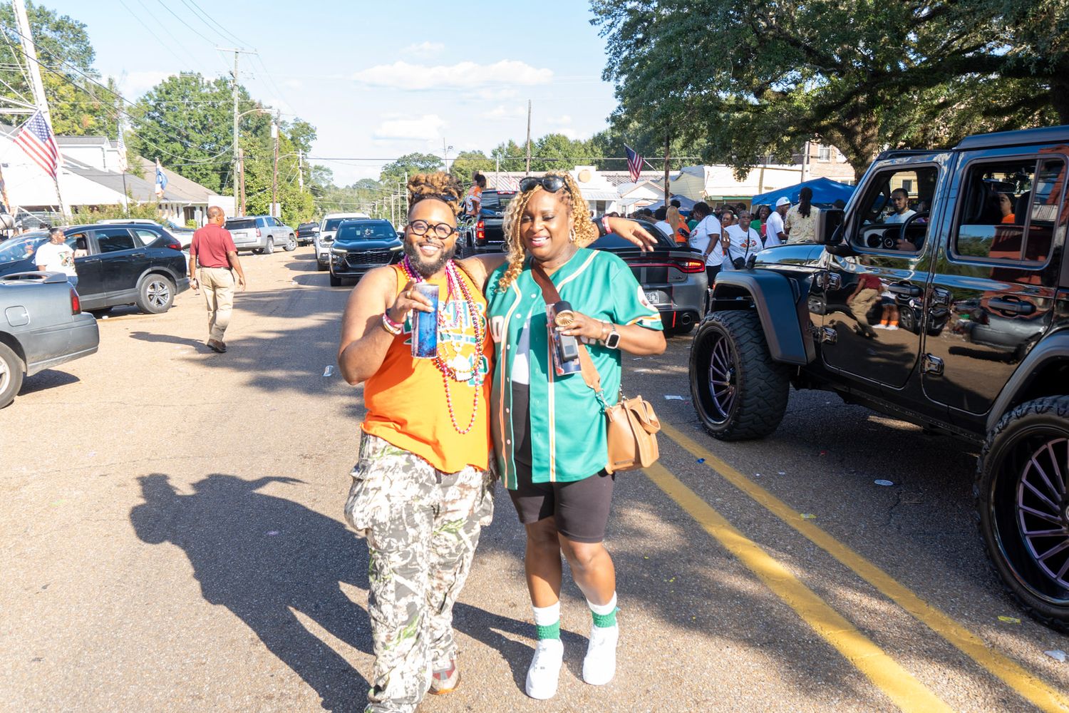 People enjoying an outdoor community gathering with blue tents and parked cars in the background.