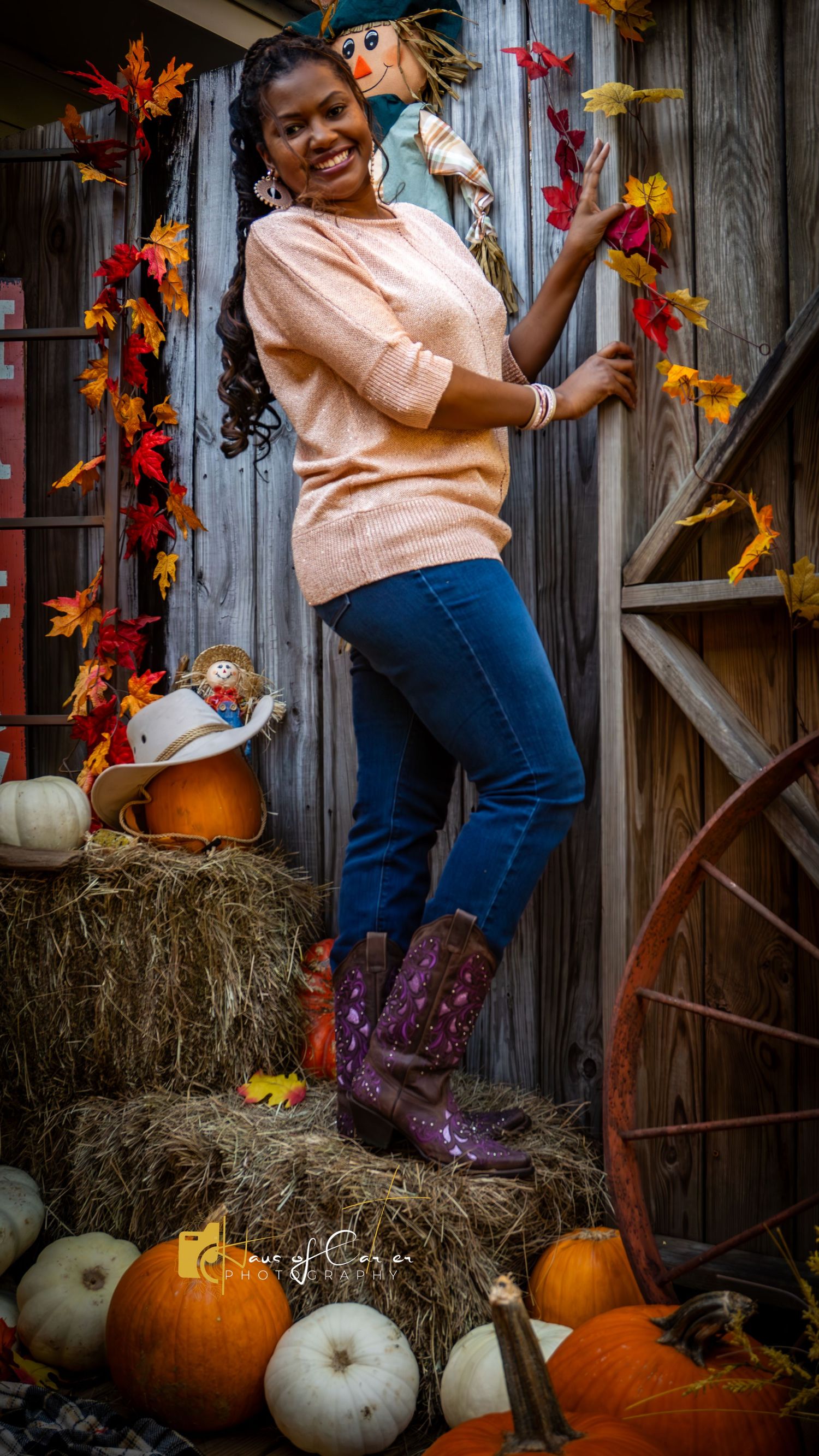 Casual fall photoshoot scene with pumpkins, hay bales and autumn leaves against rustic wooden background.