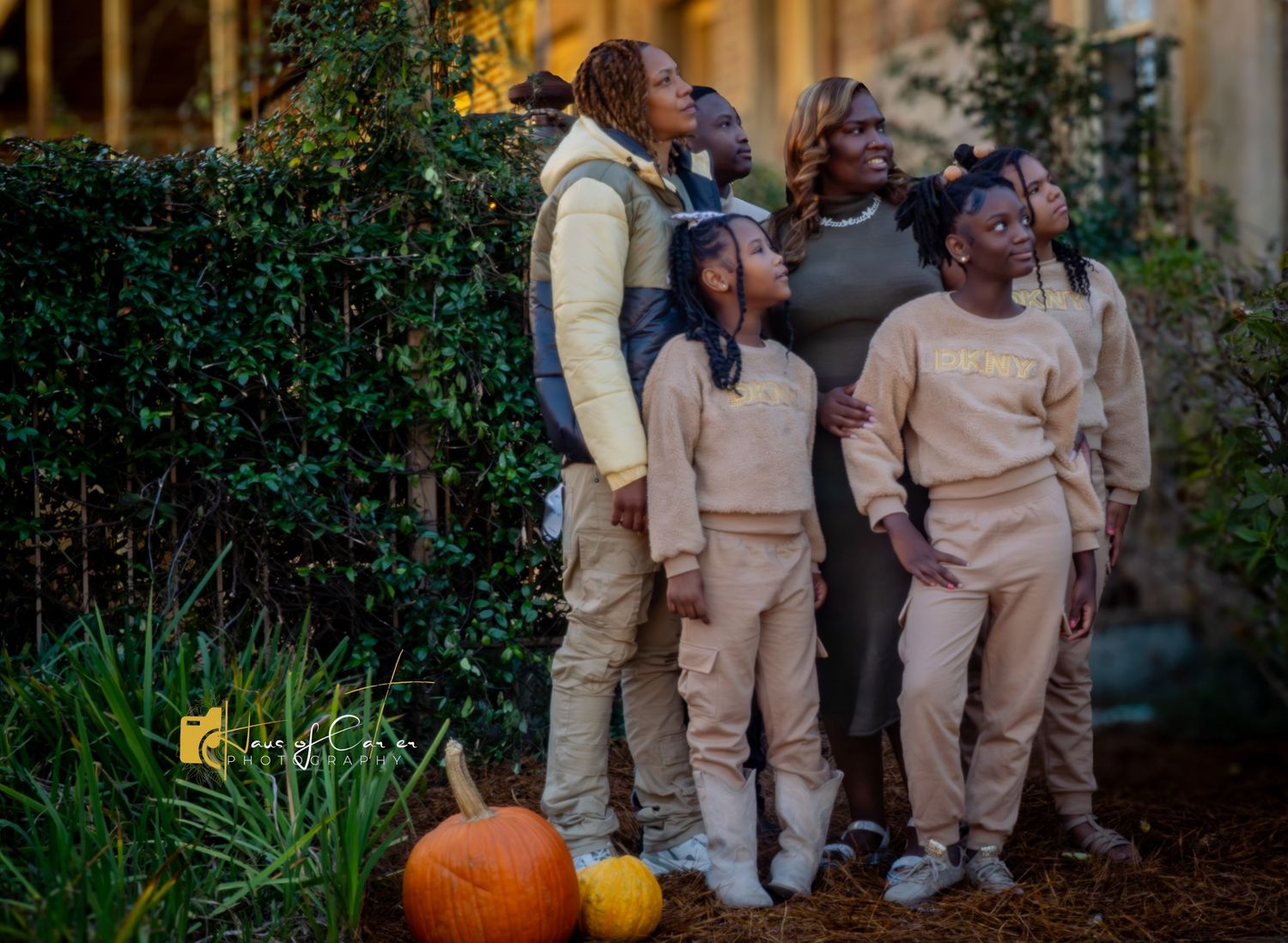 Family group wearing matching beige outfits posing outdoors with autumn pumpkin decorations.