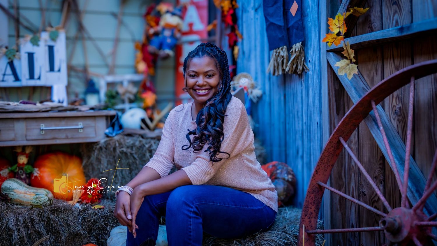 Festive fall photography setup featuring orange pumpkins, straw bales and colorful autumn leaves against blue backdrop.