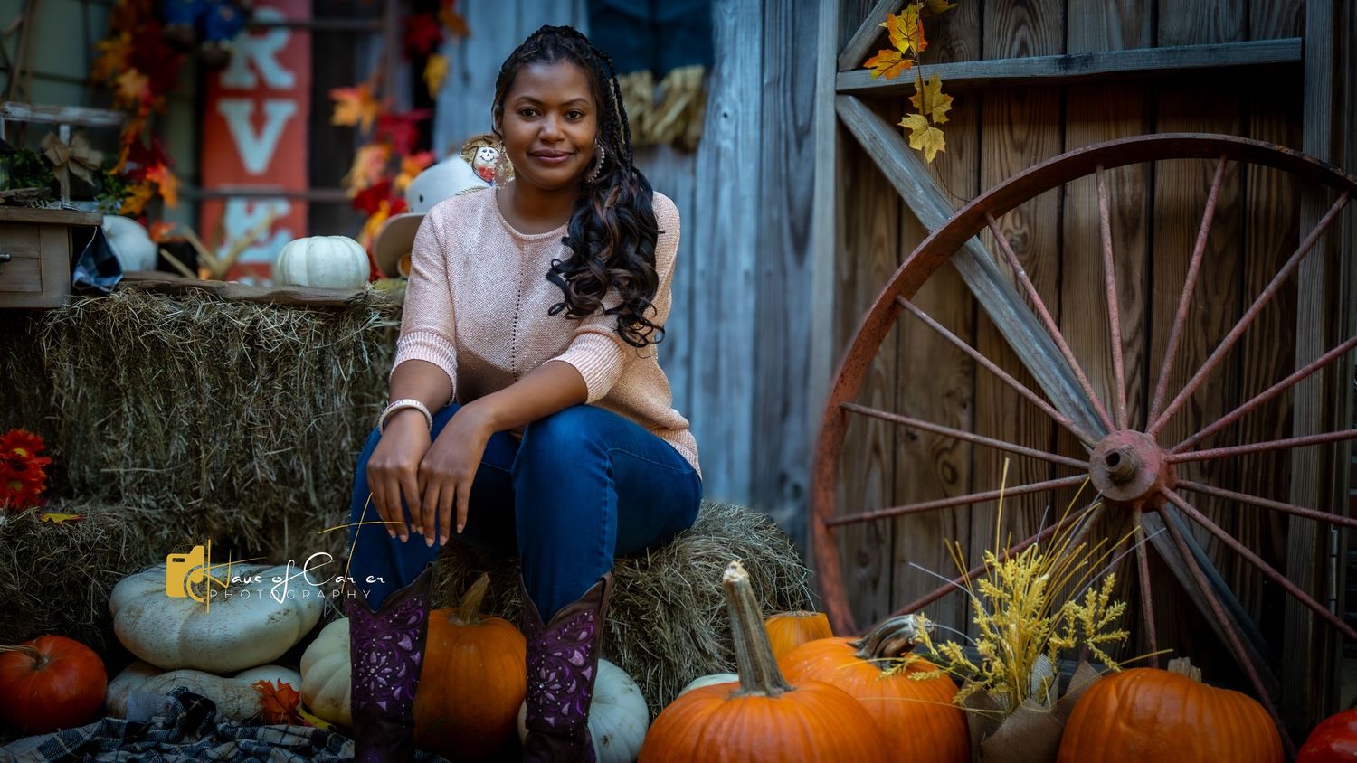 Autumn portrait session with pumpkins, hay bales and fall foliage decorations in front of weathered blue barn.