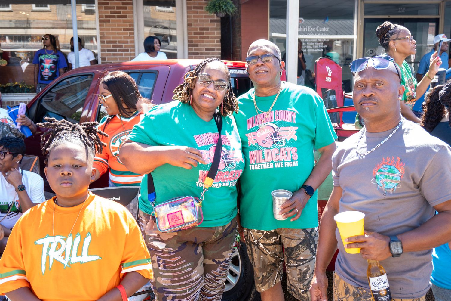 Fans in teal and orange jerseys celebrating at an outdoor gathering with drinks and smiles.