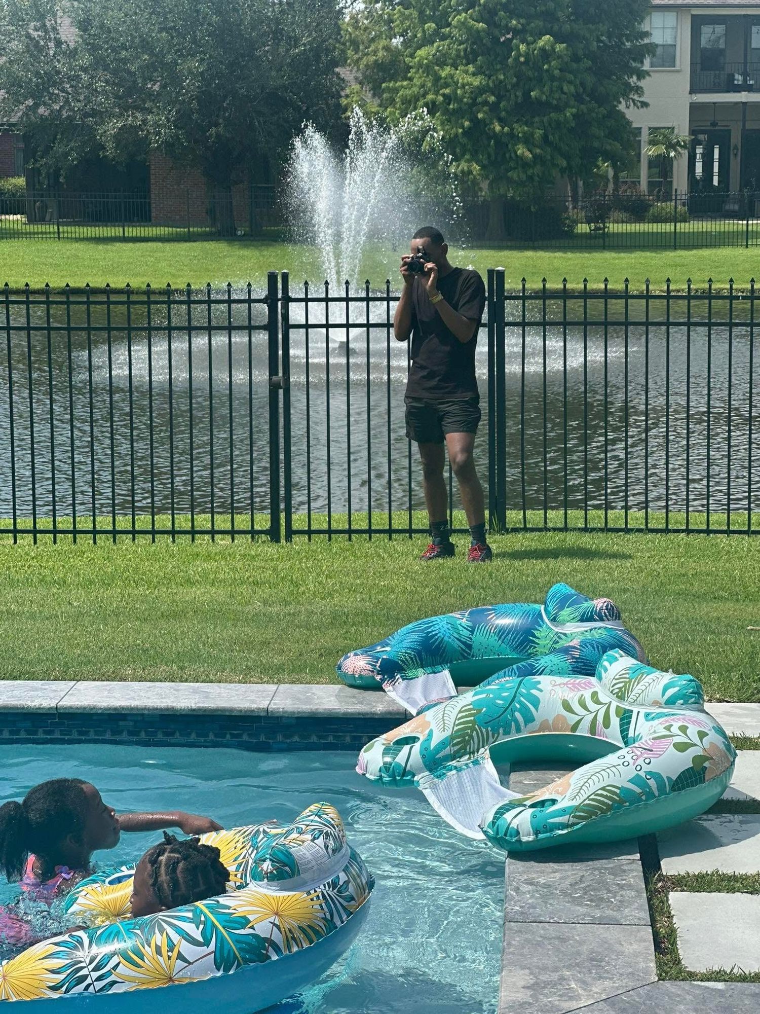 Four sequential photos show someone relaxing on a tropical print pool float near a fountain in a backyard setting.