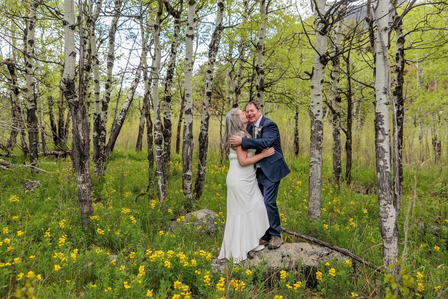 Couple embracing in spring birch forest with yellow wildflowers blooming on forest floor.
