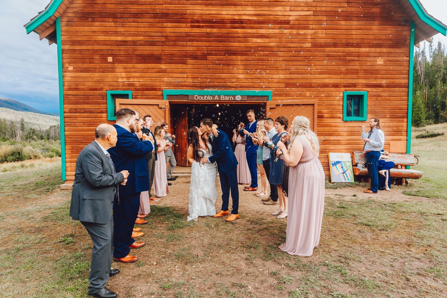 Rustic log cabin with teal trim serves as backdrop for outdoor gathering in mountain setting.