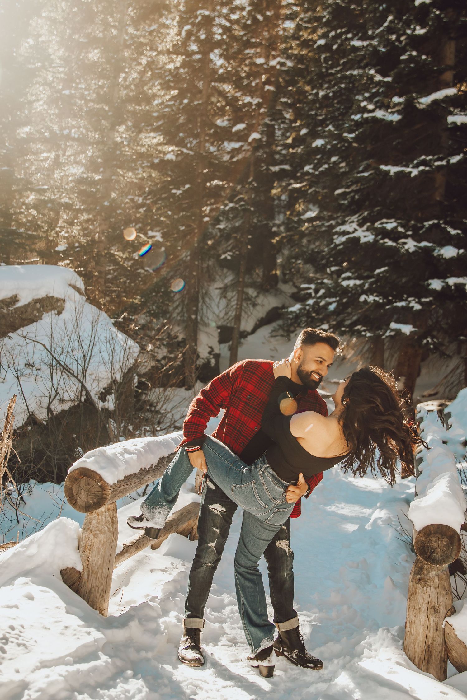 A romantic winter scene with couple embracing among snow-covered logs in sunlit forest.