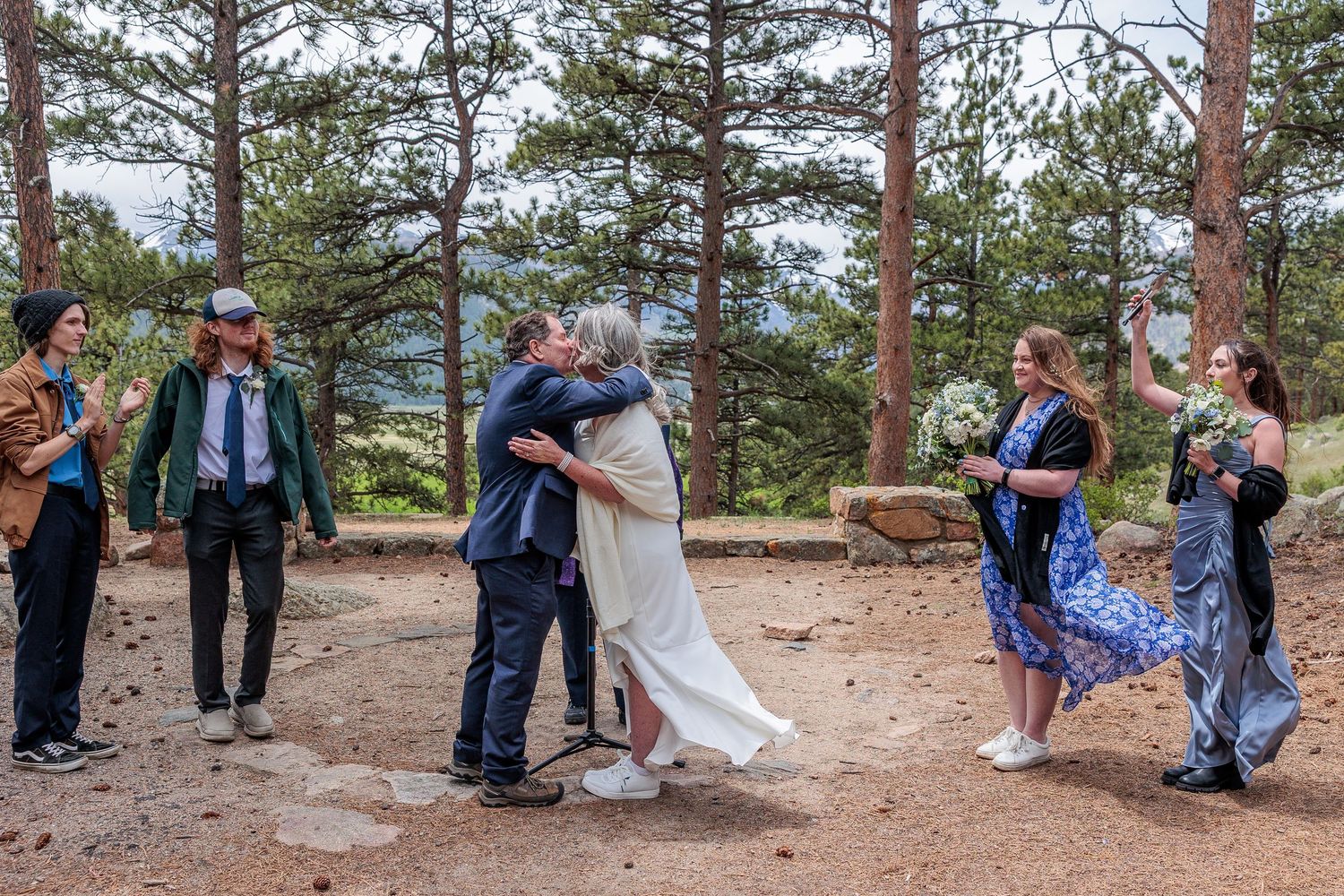 A wedding ceremony takes place in a scenic mountain forest setting with tall pine trees and natural surroundings.