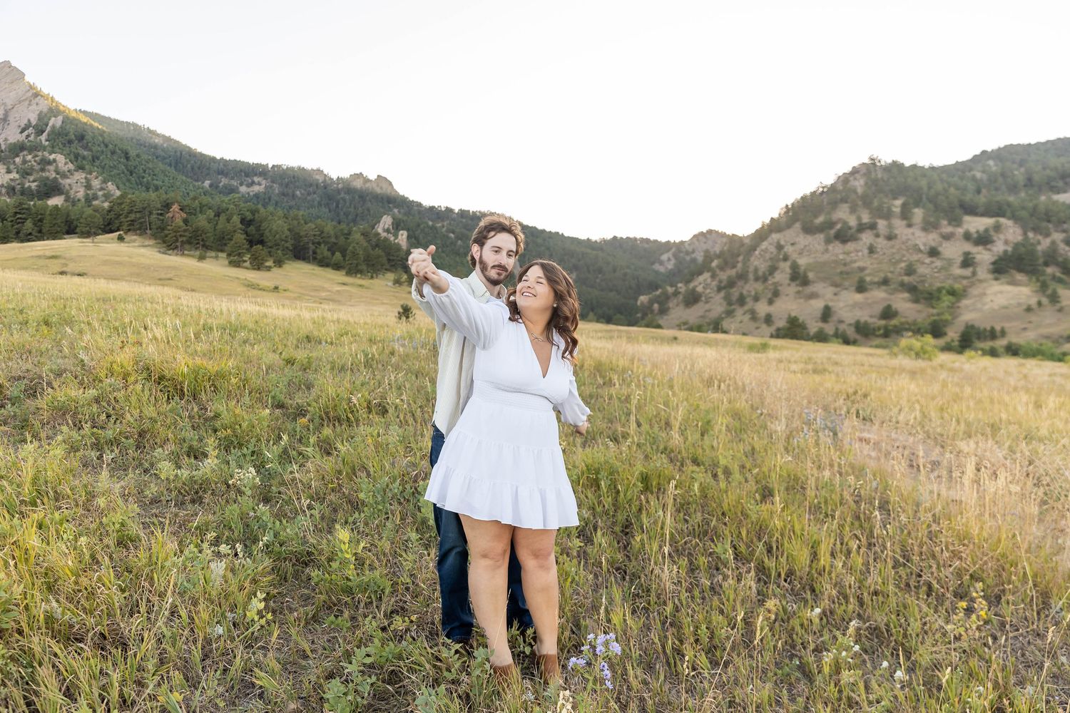 A couple embraces in a scenic mountain meadow filled with wildflowers during golden hour.