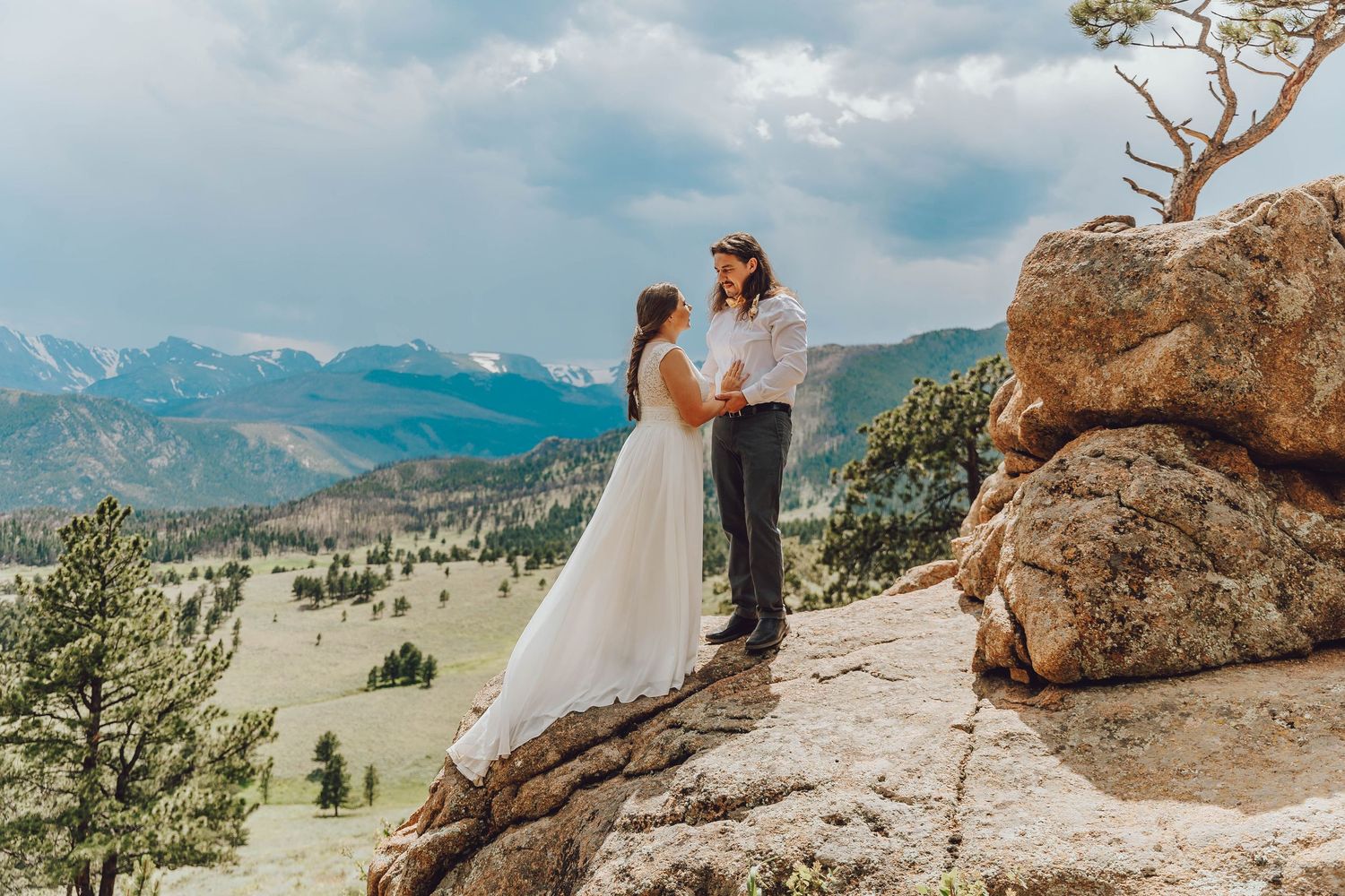 A couple shares an intimate moment on a rocky mountain overlook with panoramic valley views.