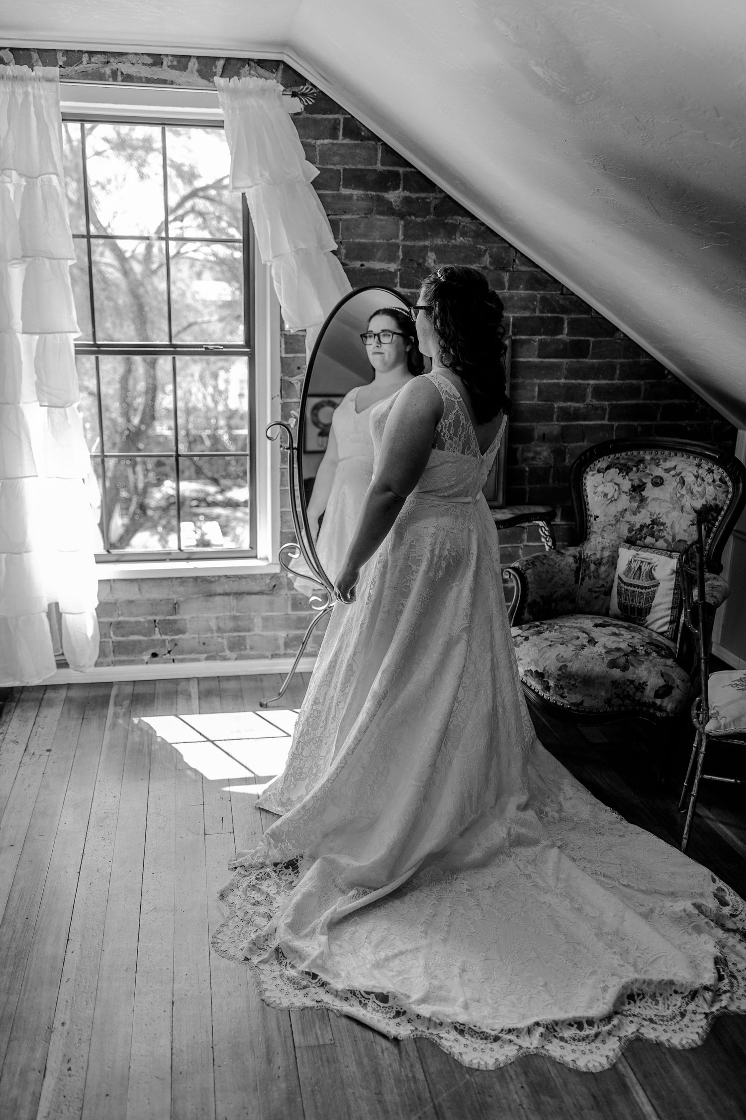 A bride in a flowing white wedding gown twirls gracefully in an attic room with exposed brick walls and sunlit windows in Tuscon Arizona