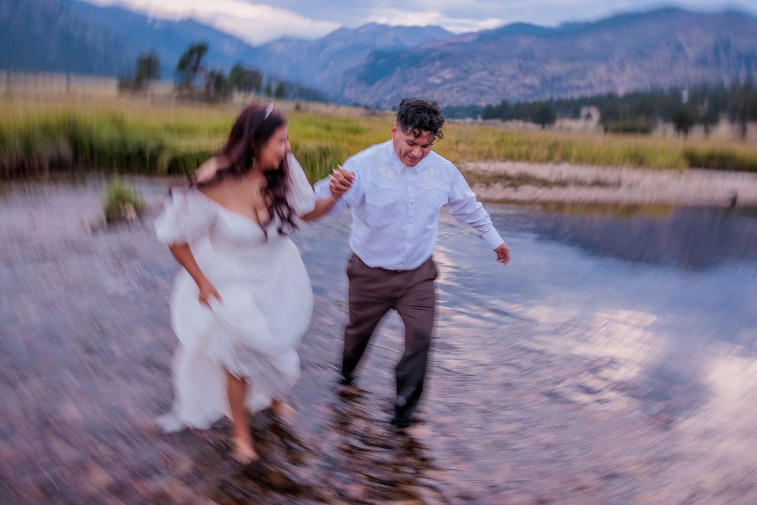 A couple splashes playfully in mountain lake waters during their wedding photo session.