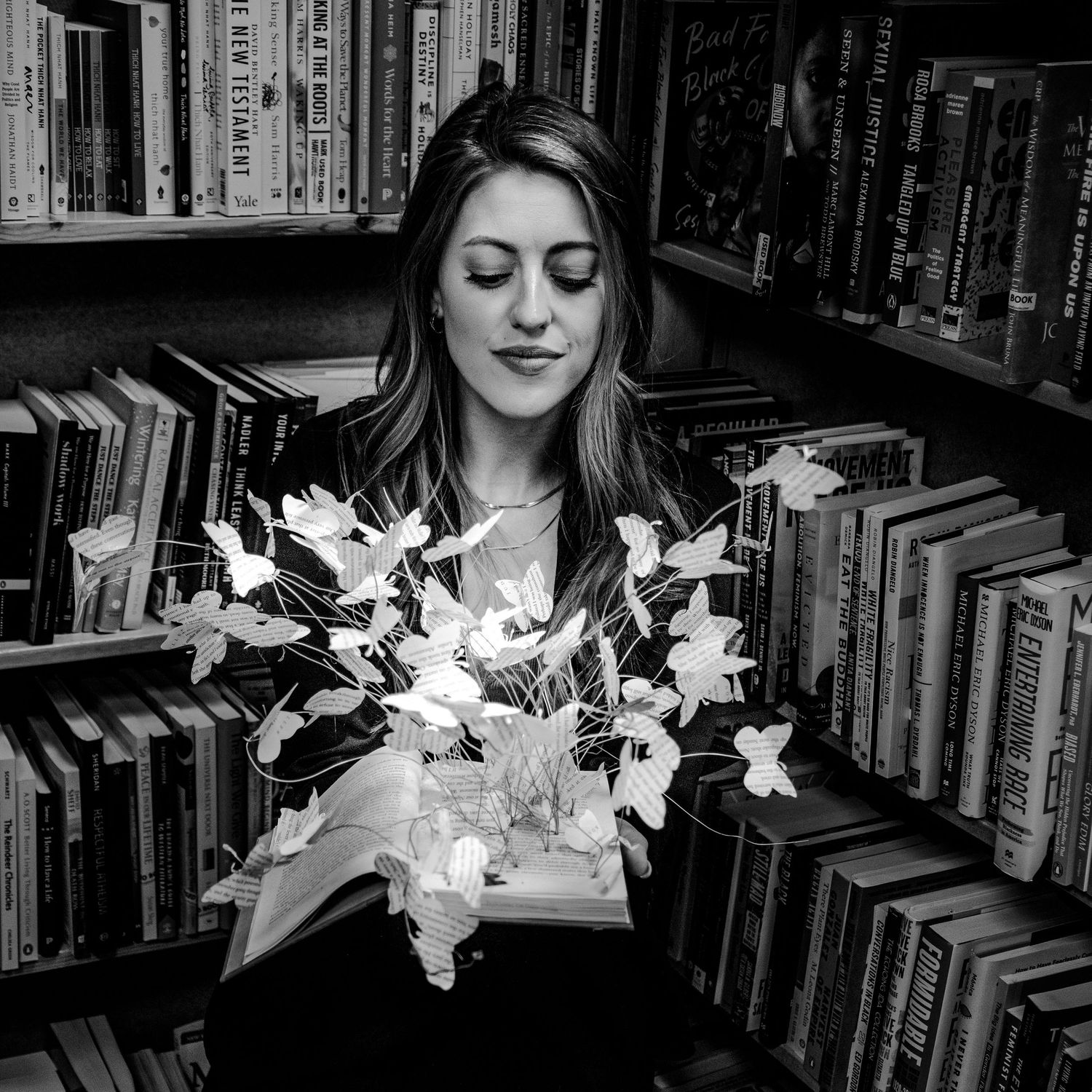 Black and white image of a person surrounded by bookshelves with glowing butterfly lights creating a magical effect.