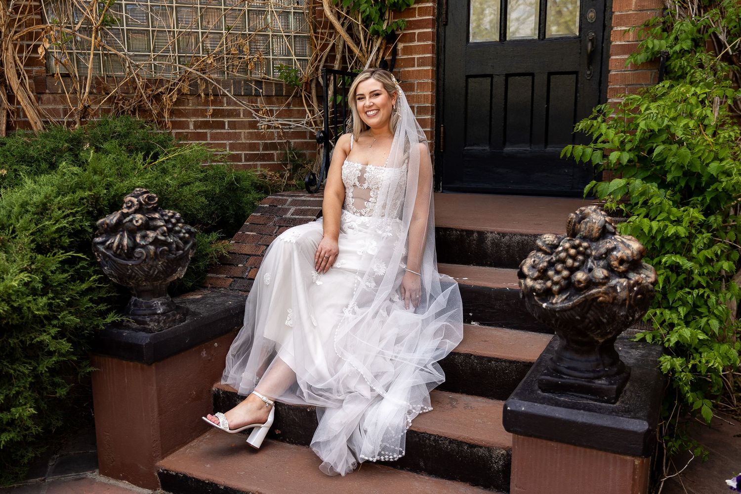Bridal portraits on brick steps with elegant white dress and garden backdrop.