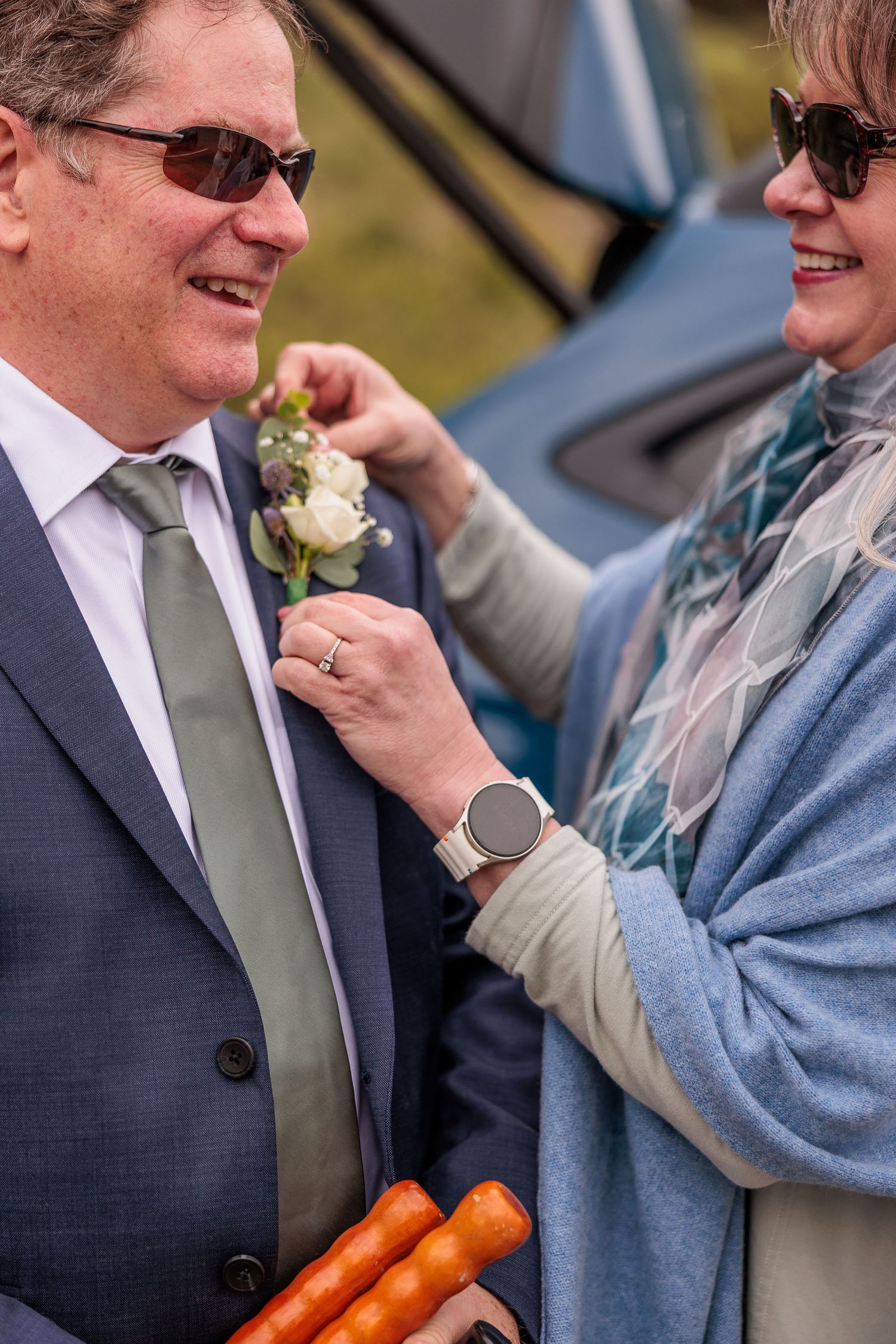 A boutonniere being pinned onto a navy suit jacket at an outdoor event.