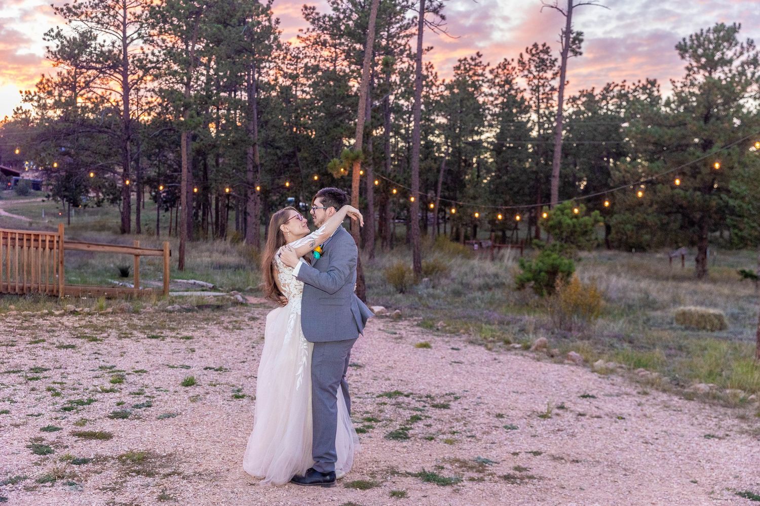 Couple sharing romantic moments during sunset in a forest setting with string lights creating a magical atmosphere.