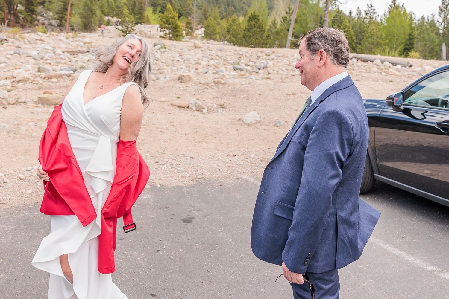 A couple in formal attire walks together on a rocky outdoor path during a wedding photo session.
