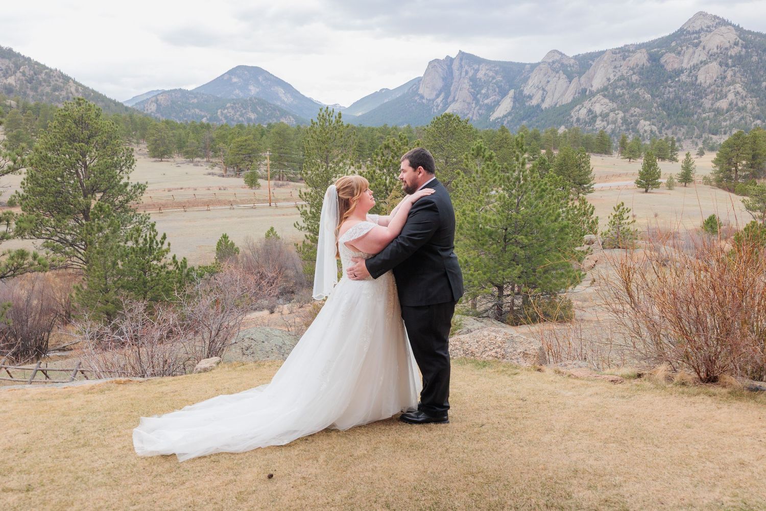 Bride and groom share a romantic embrace with stunning Rocky Mountain peaks and pine trees in the background.