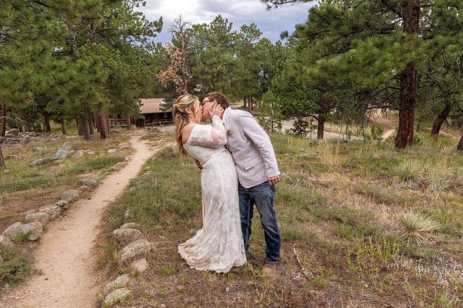 A couple strolls along a winding dirt path through a scenic mountain landscape.