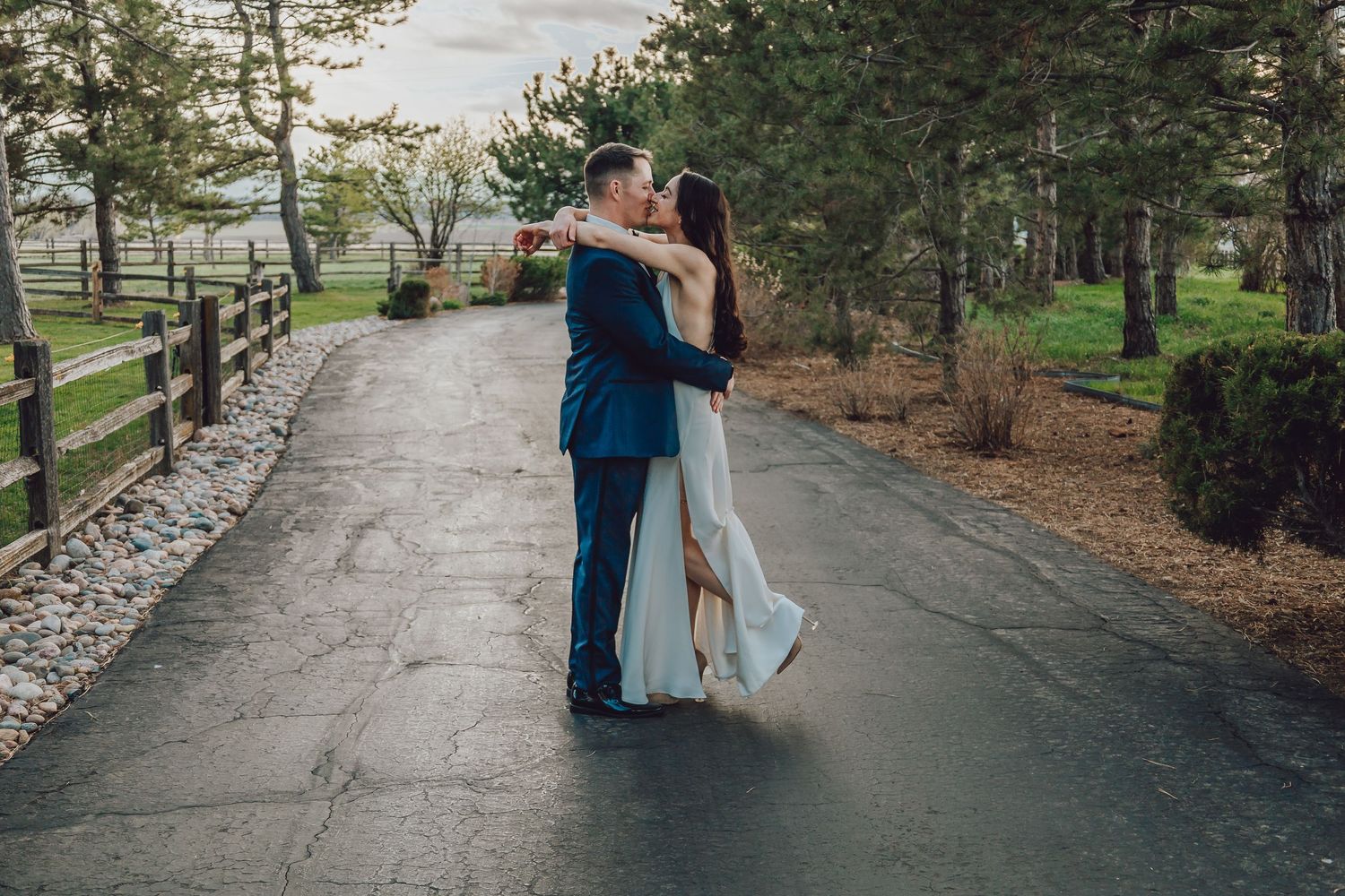 Couple embracing on a paved pathway surrounded by evergreen trees.