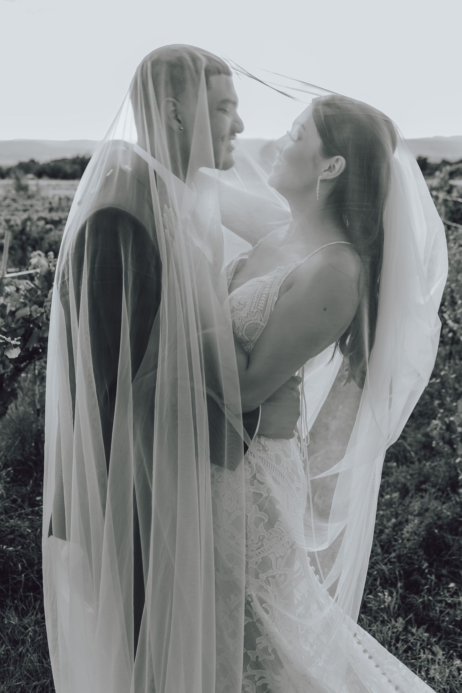 A romantic black and white wedding photo series showing a couple embracing under a flowing veil in an outdoor setting.