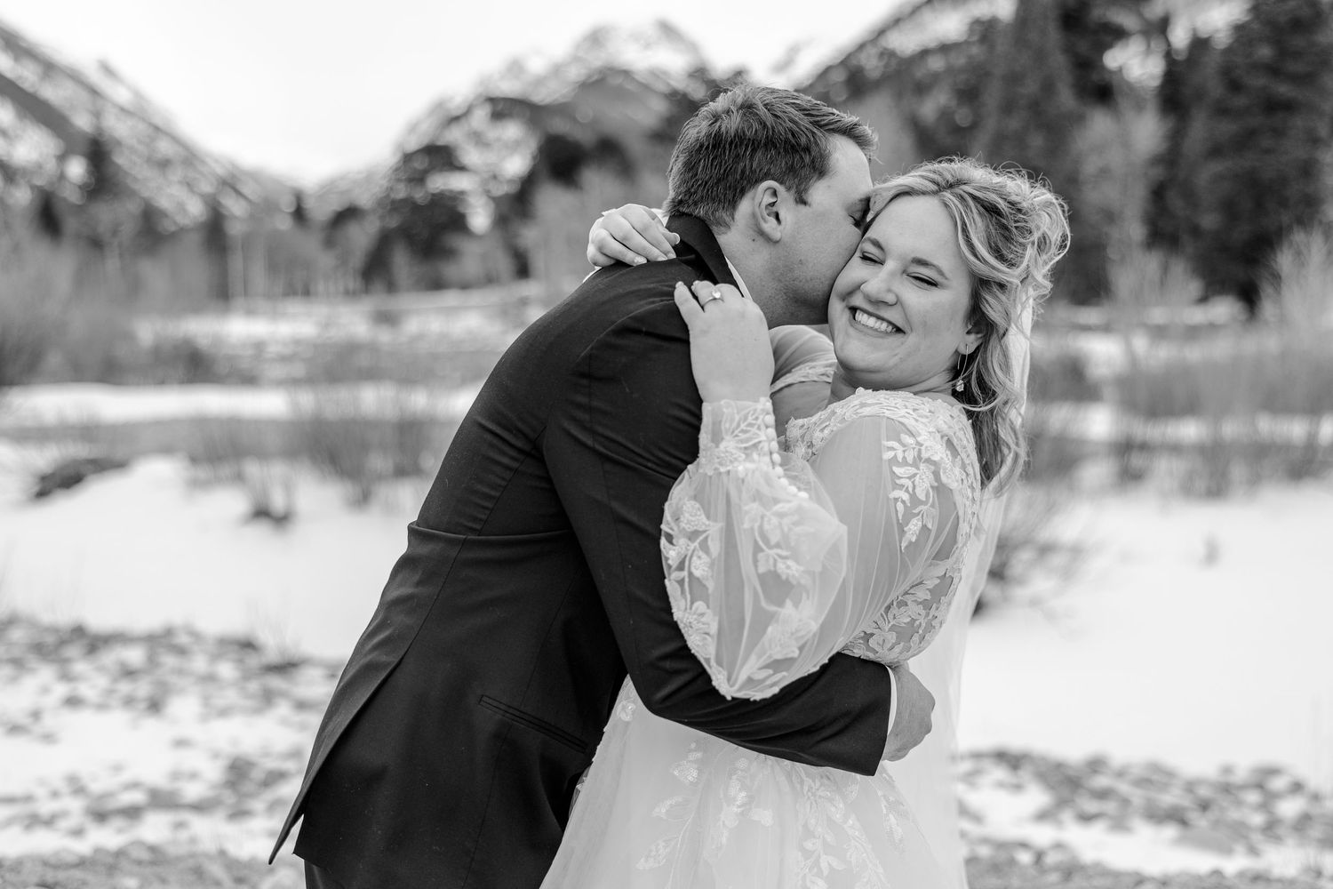 A couple embraces in a romantic kiss during their winter wedding photoshoot in a snowy outdoor setting.