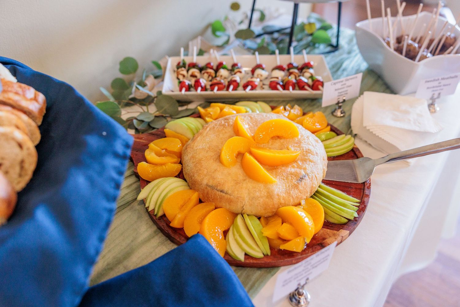 Wedding reception table with colorful fruit platters and desserts arranged on blue tablecloths.