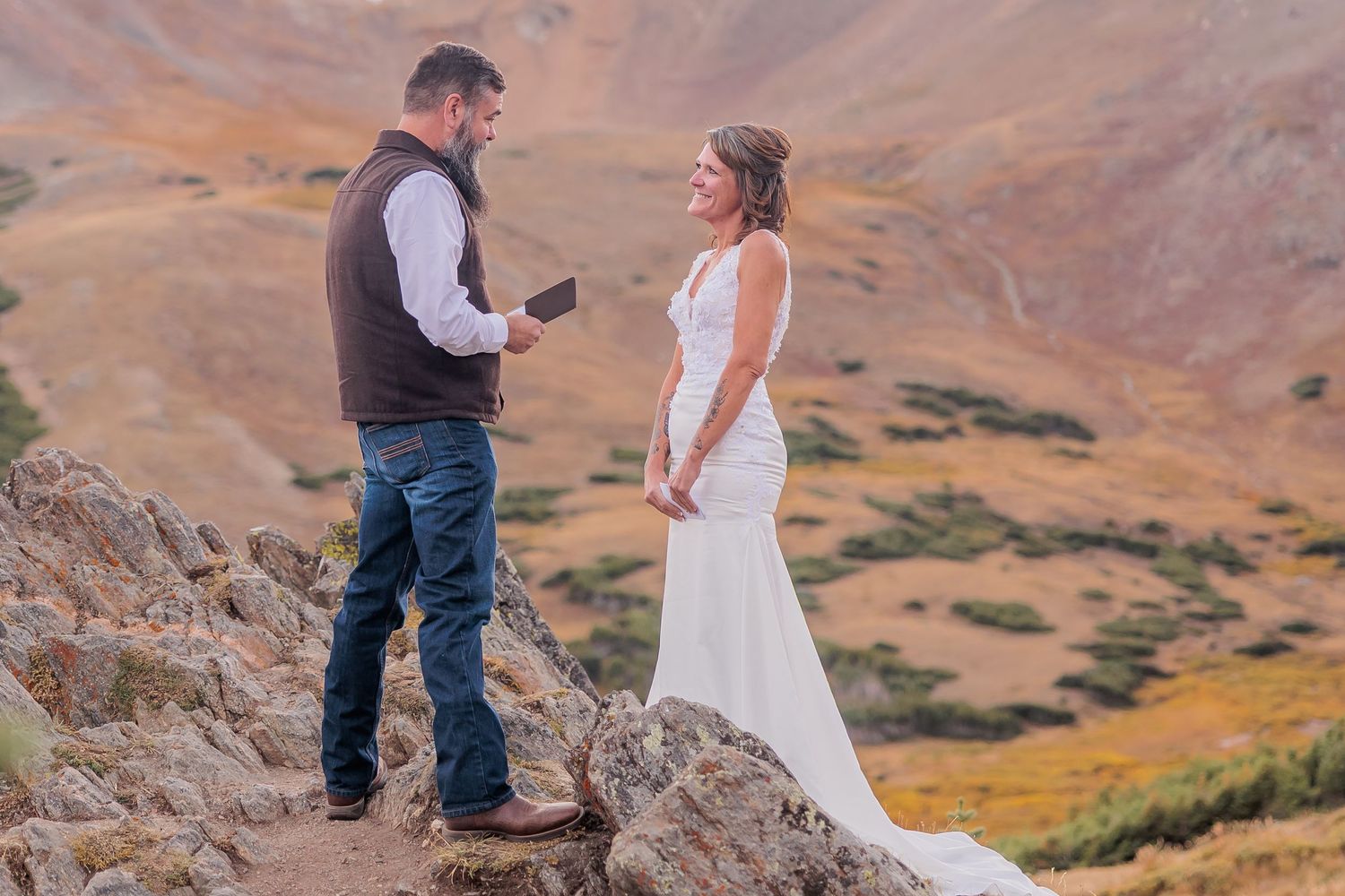 Two people share an intimate moment while standing on a mountain ridge with desert landscape in the background.