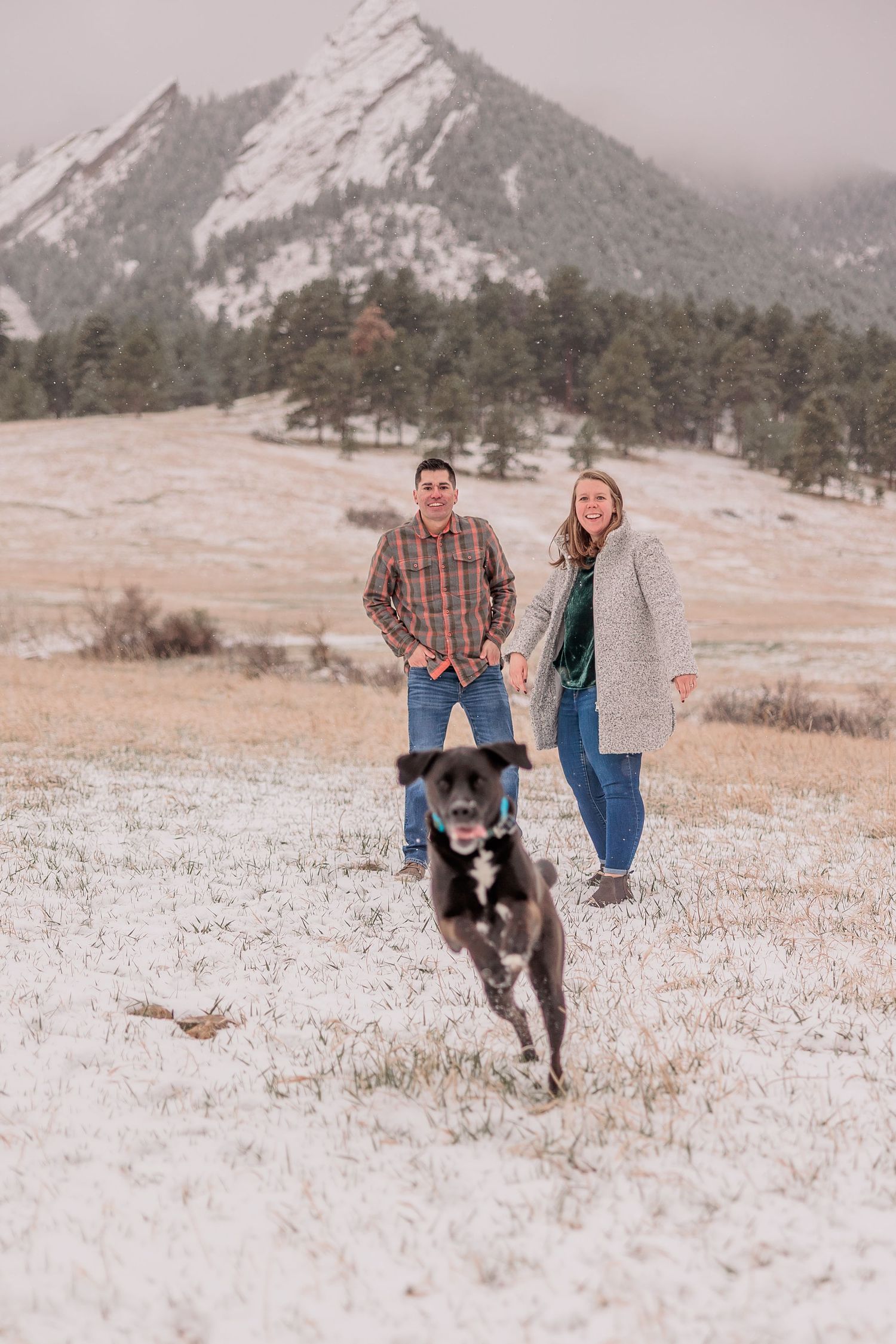 A couple and their husky dog playing together in a snowy mountain landscape during winter.