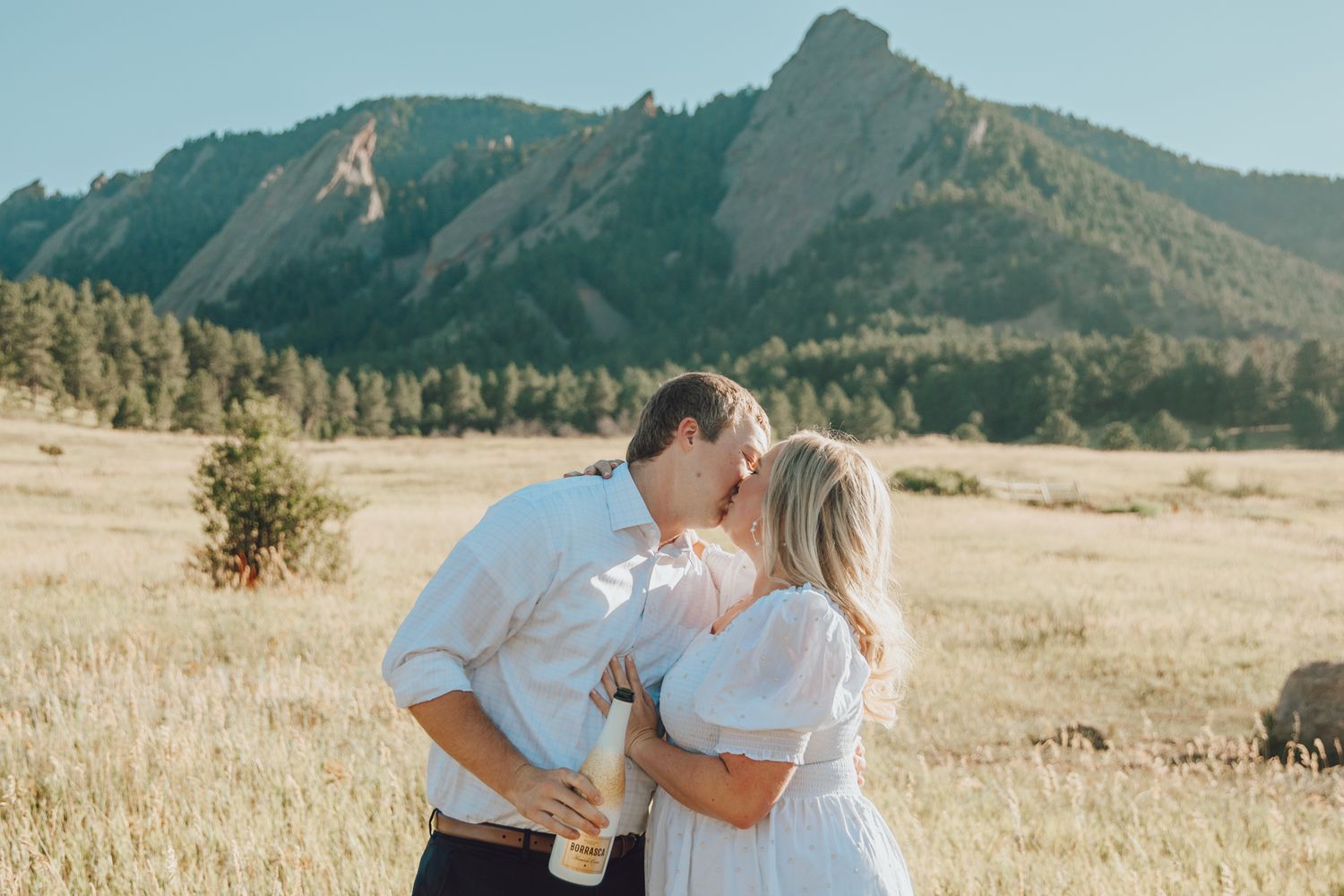 A romantic moment between a couple in a golden field with mountains rising dramatically in the background.